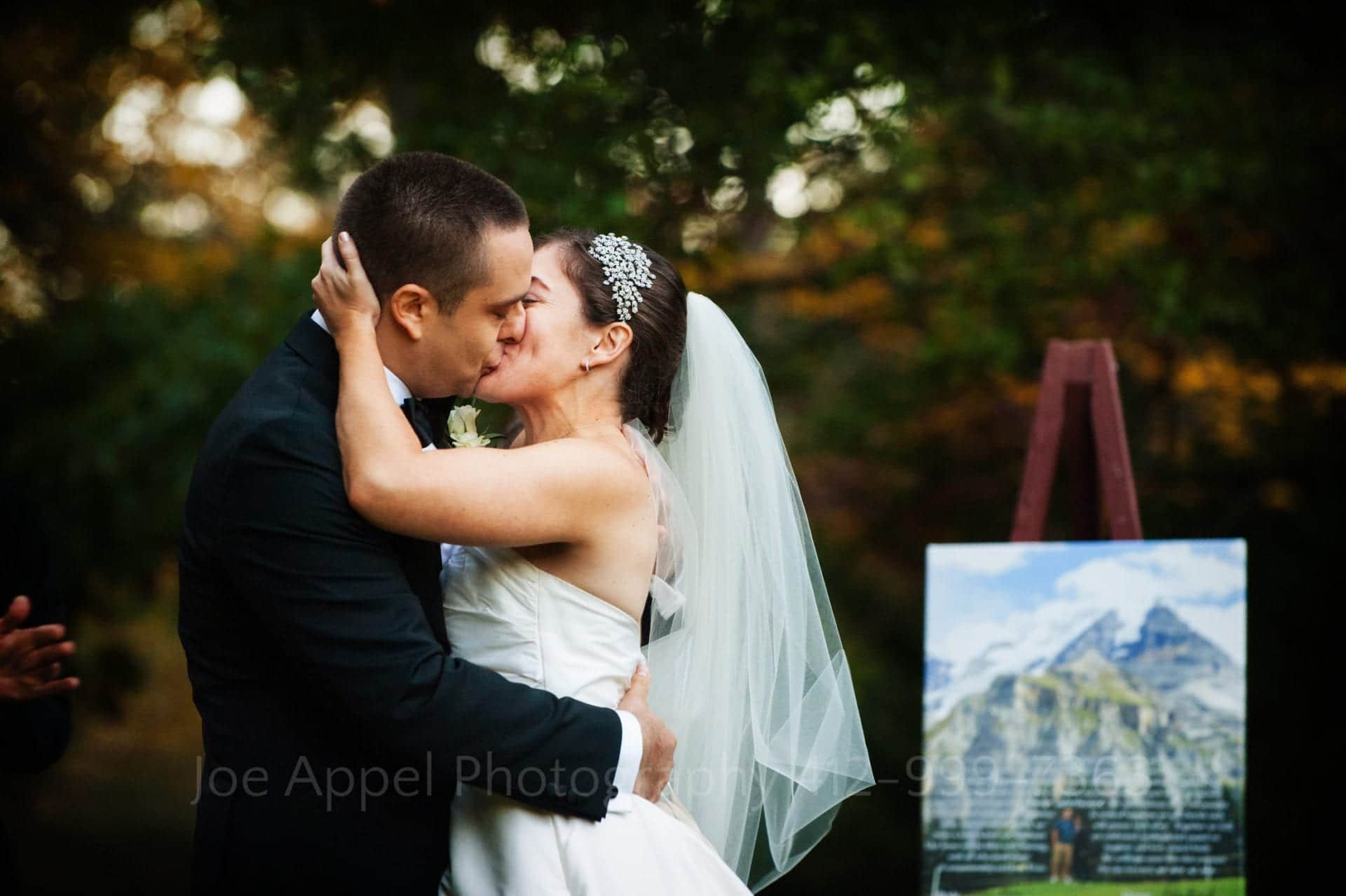a bride and groom kiss next to a painting of a mountain Seven Springs Weddings