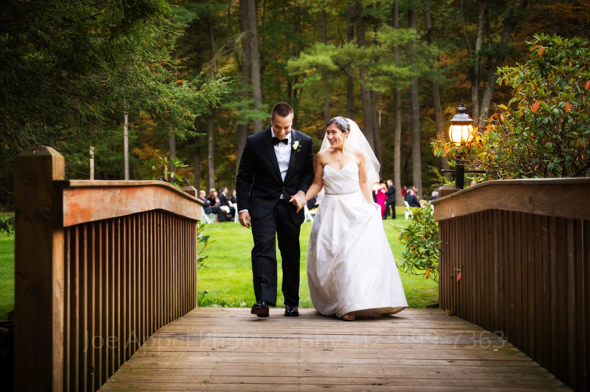 a bride and groom hold hands and walk across a wooden bridge Seven Springs Weddings