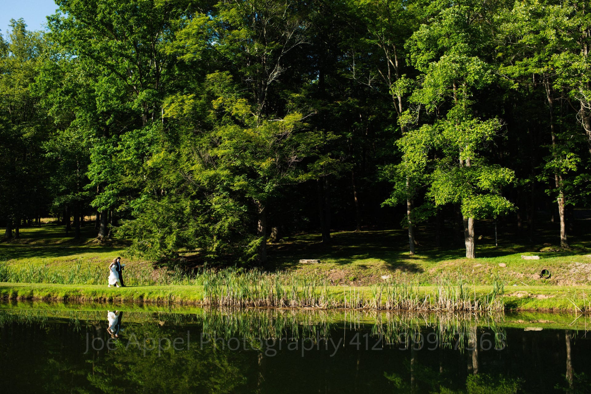 a bride and groom walk on the grass by a lake Seven Springs Weddings