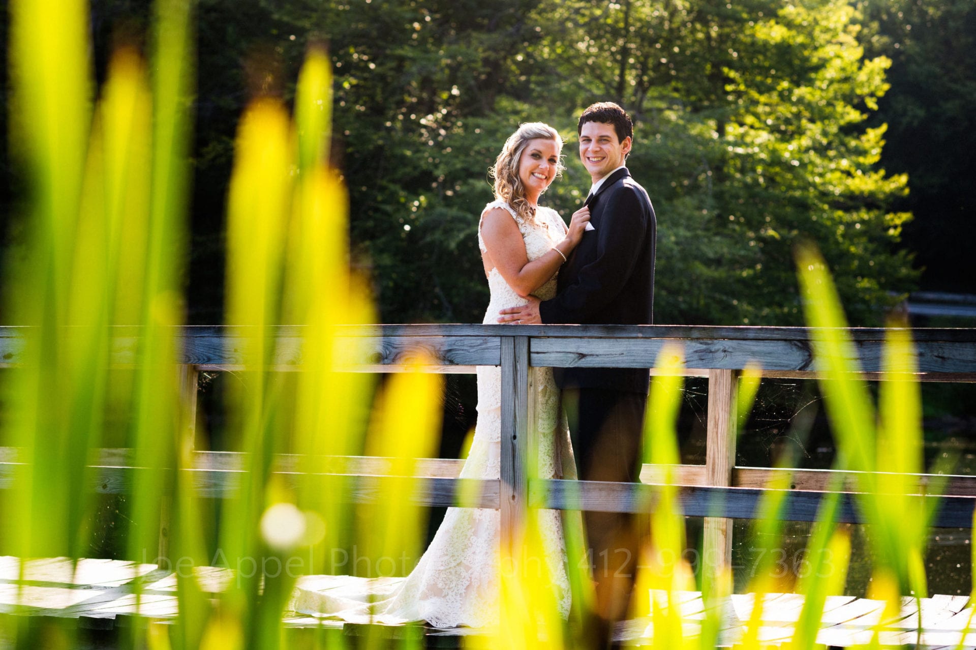 a bride and groom smile and pose on a wooden bridge Seven Springs Weddings