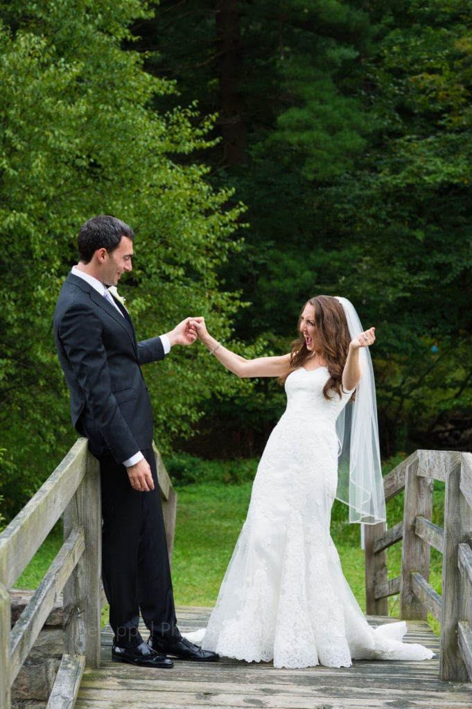 A bride and groom stand on a bridge and hold one hand as they smile and look at each other in their wedding clothes during a Seven Springs Resort wedding.