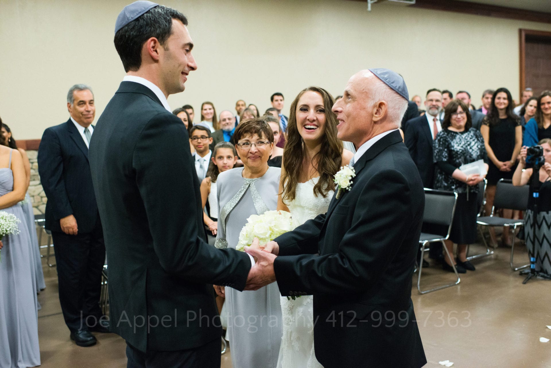 A groom shakes hands with the father of the bride as he presents his daughter to the groom.