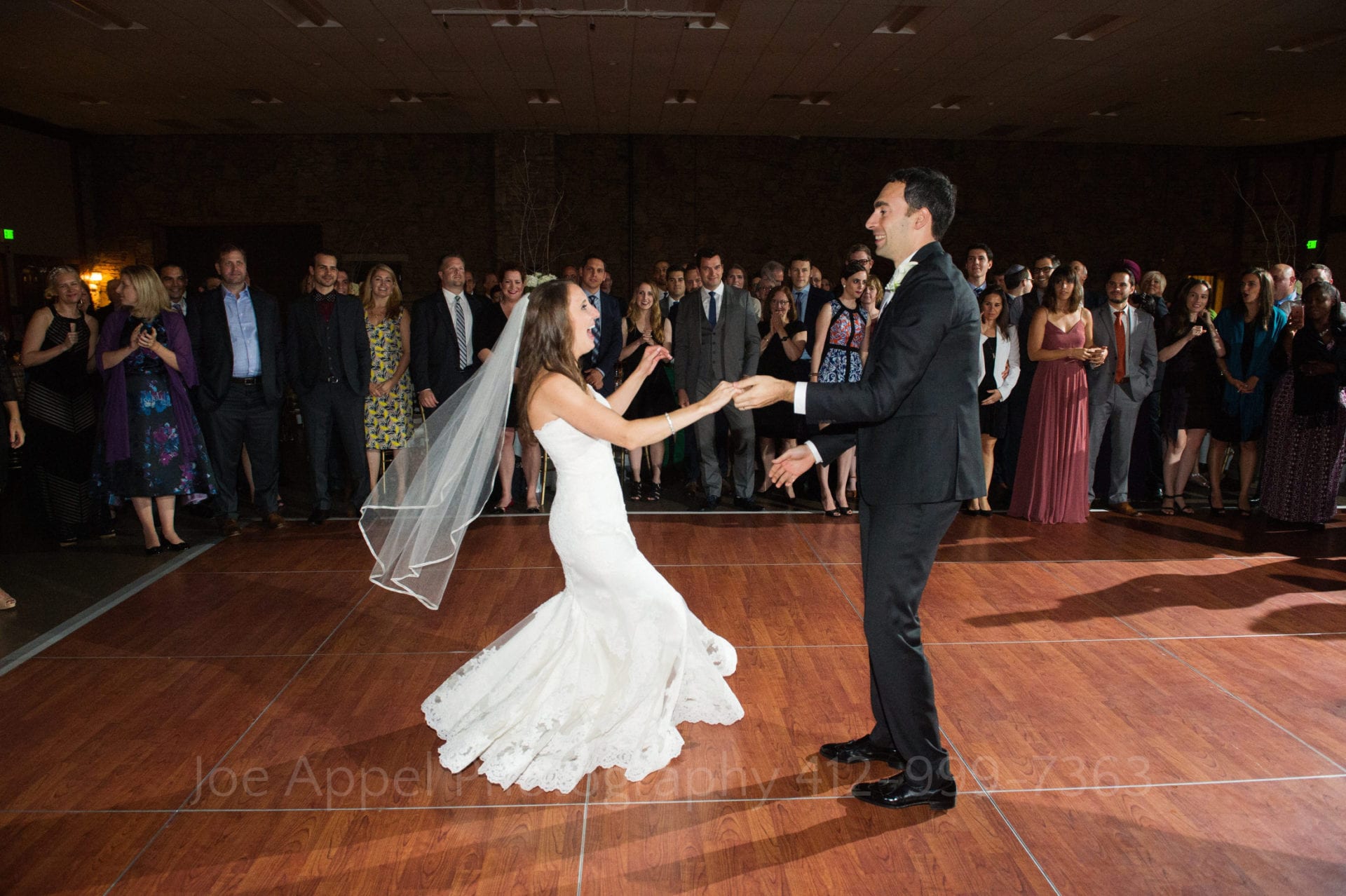 A bride and groom dance with each other in the middle of a dance floor surrounded by their guests.