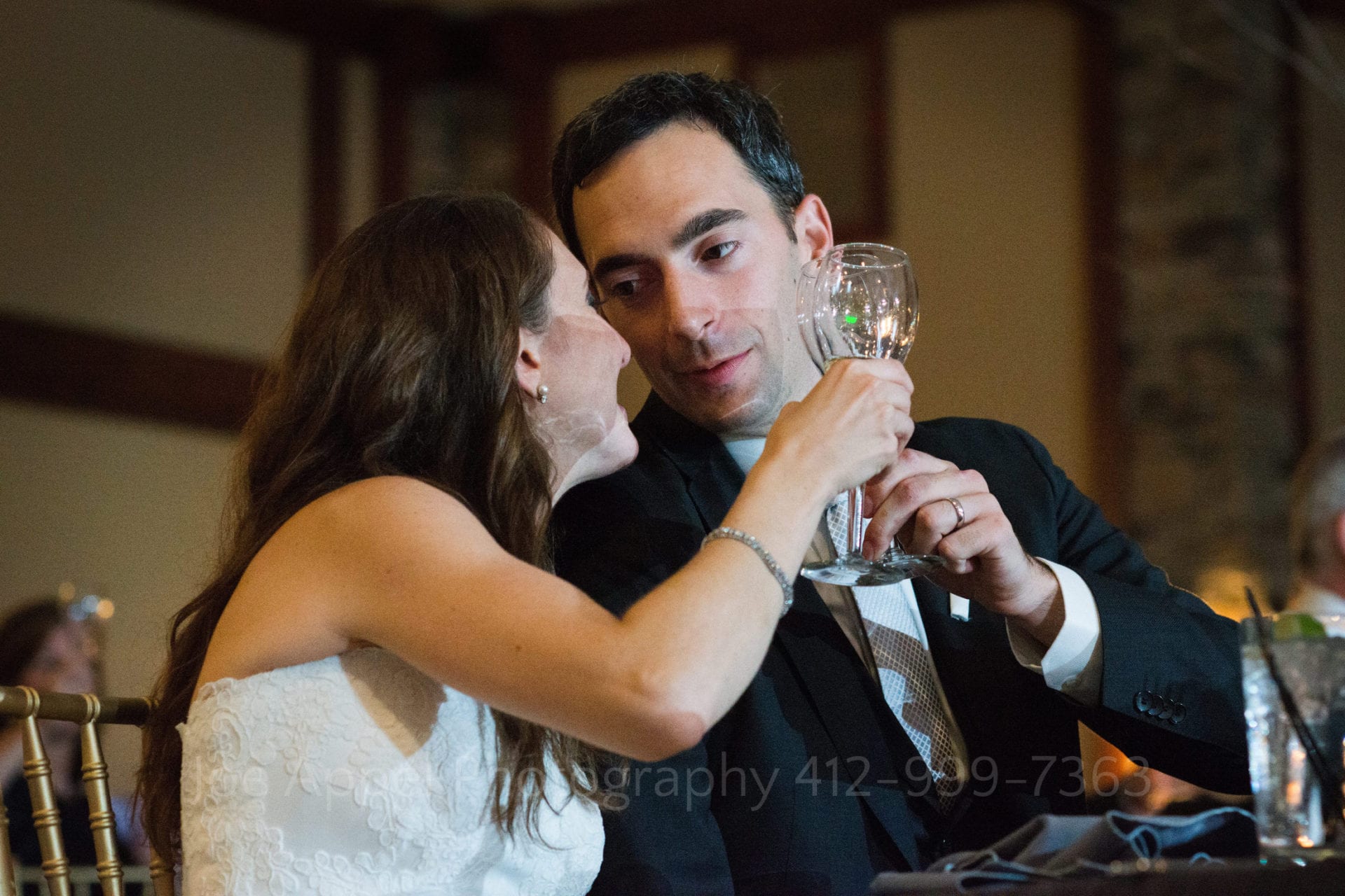 A groom looks at his bride as they sit together and touch glasses during a toast.