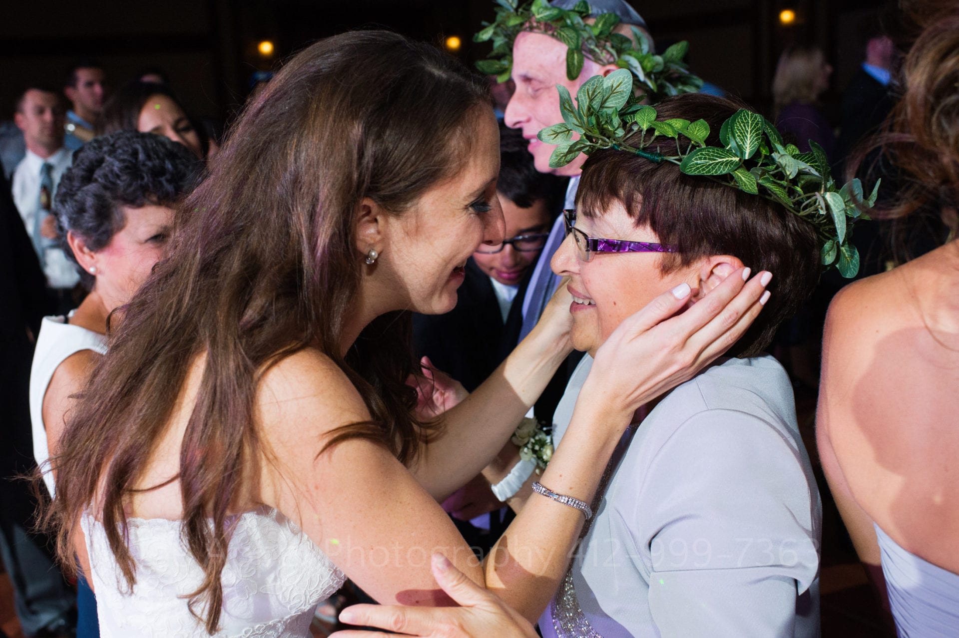 A bride caresses her mother who is wearing a laurel wreath on her head.