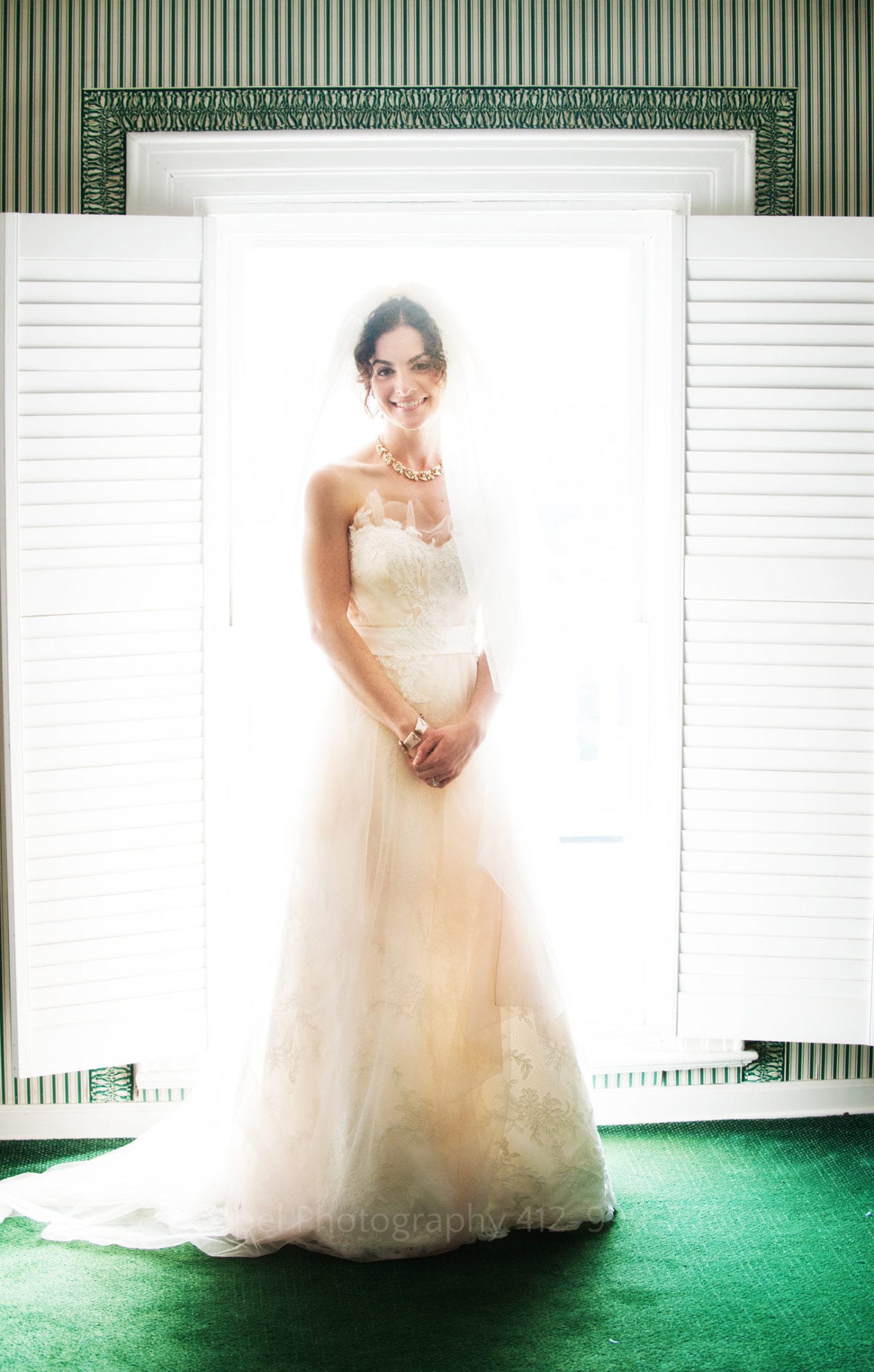 a bride smiles and stands in front of an illuminated window in her wedding dress
