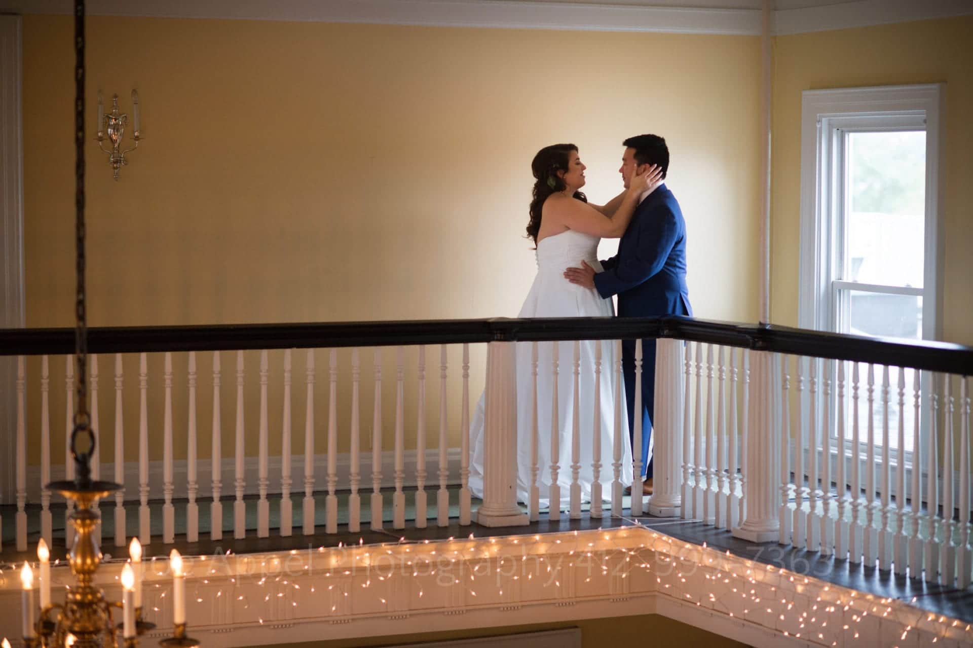 a bride and groom stand on a balcony with white fairy lights and chandeliers