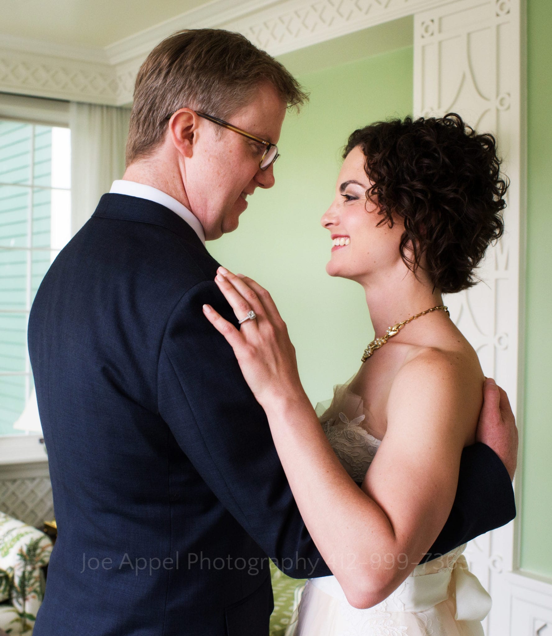 a bride and groom embrace in a green room and smile at each other