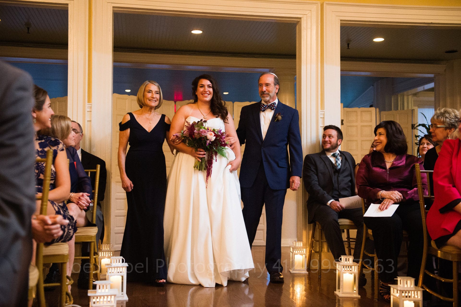 guests smile as a brides parents walk her down the aisle
