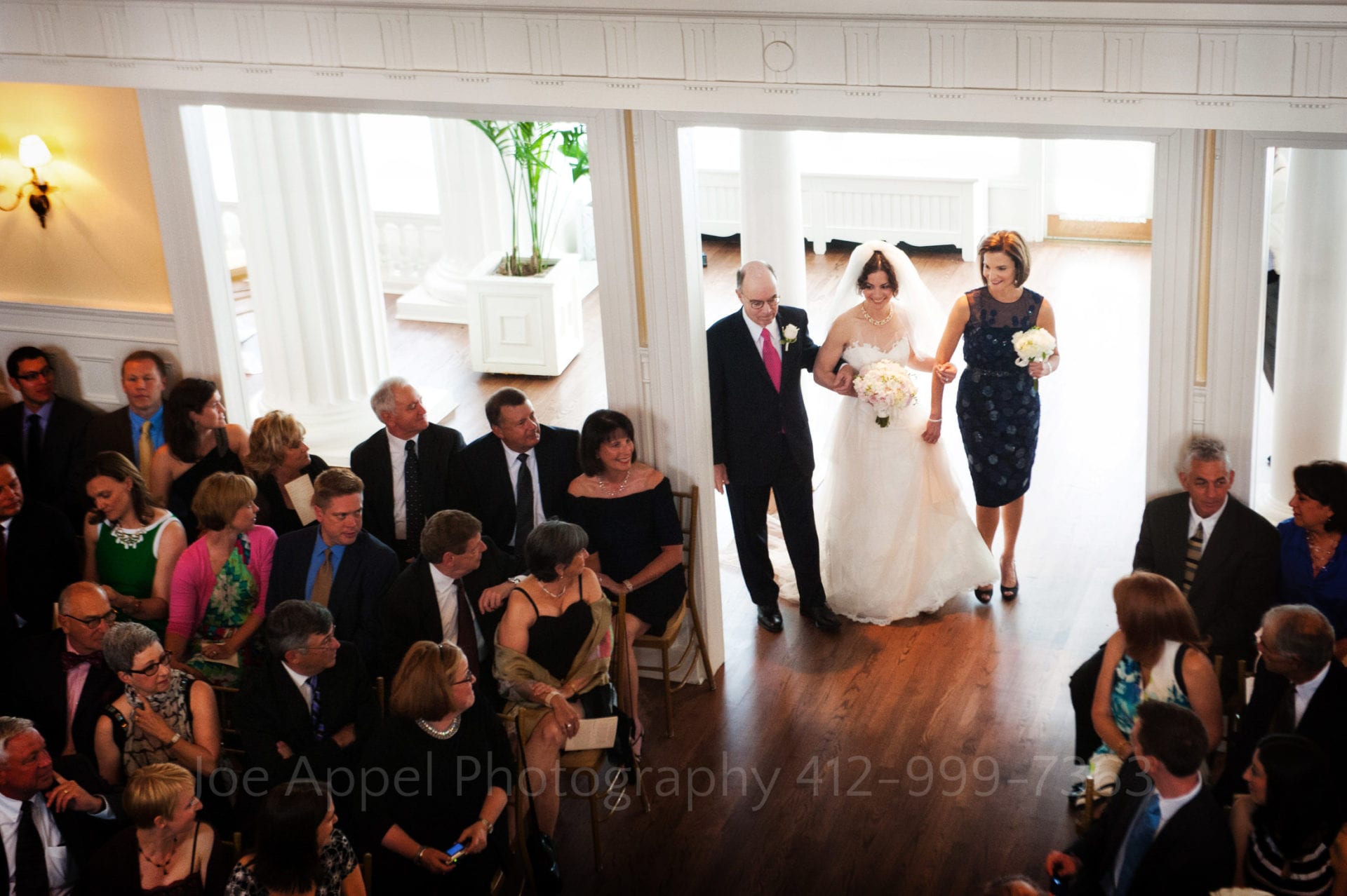 guests watch as a brides parents walk her down the aisle