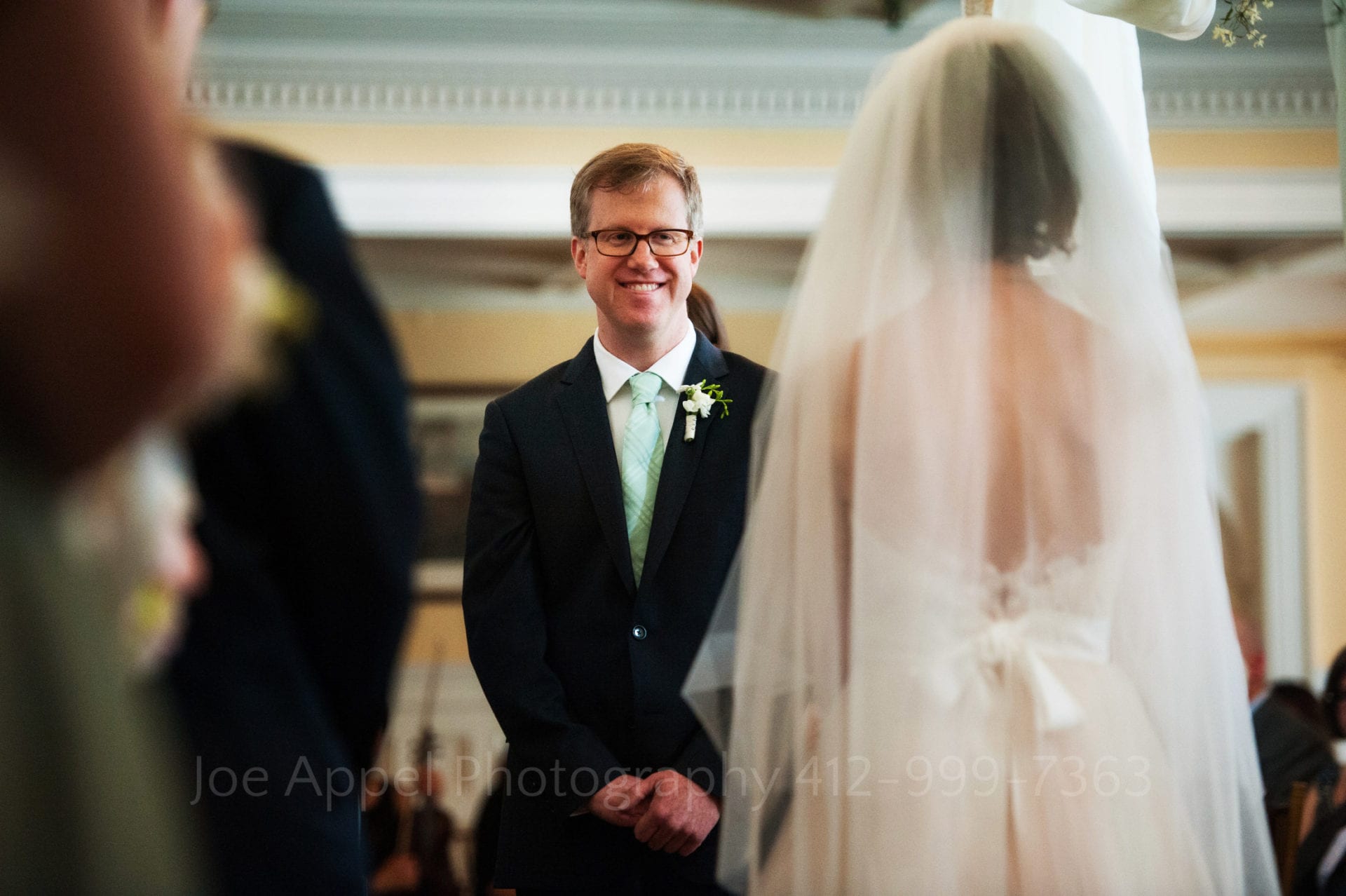a groom wearing a green tie smiles at his bride
