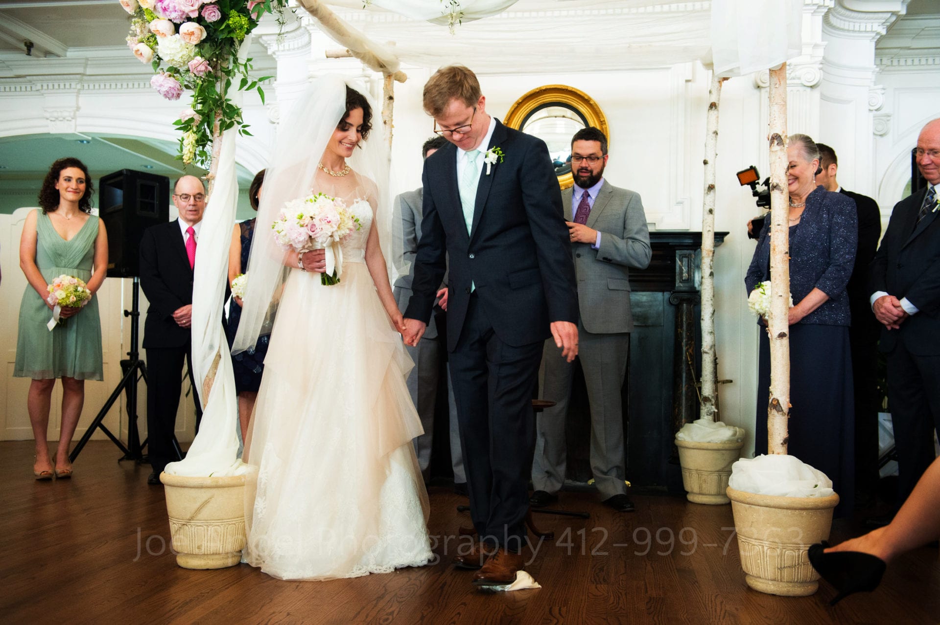 a bride holds her grooms hand as he steps on a handkerchief