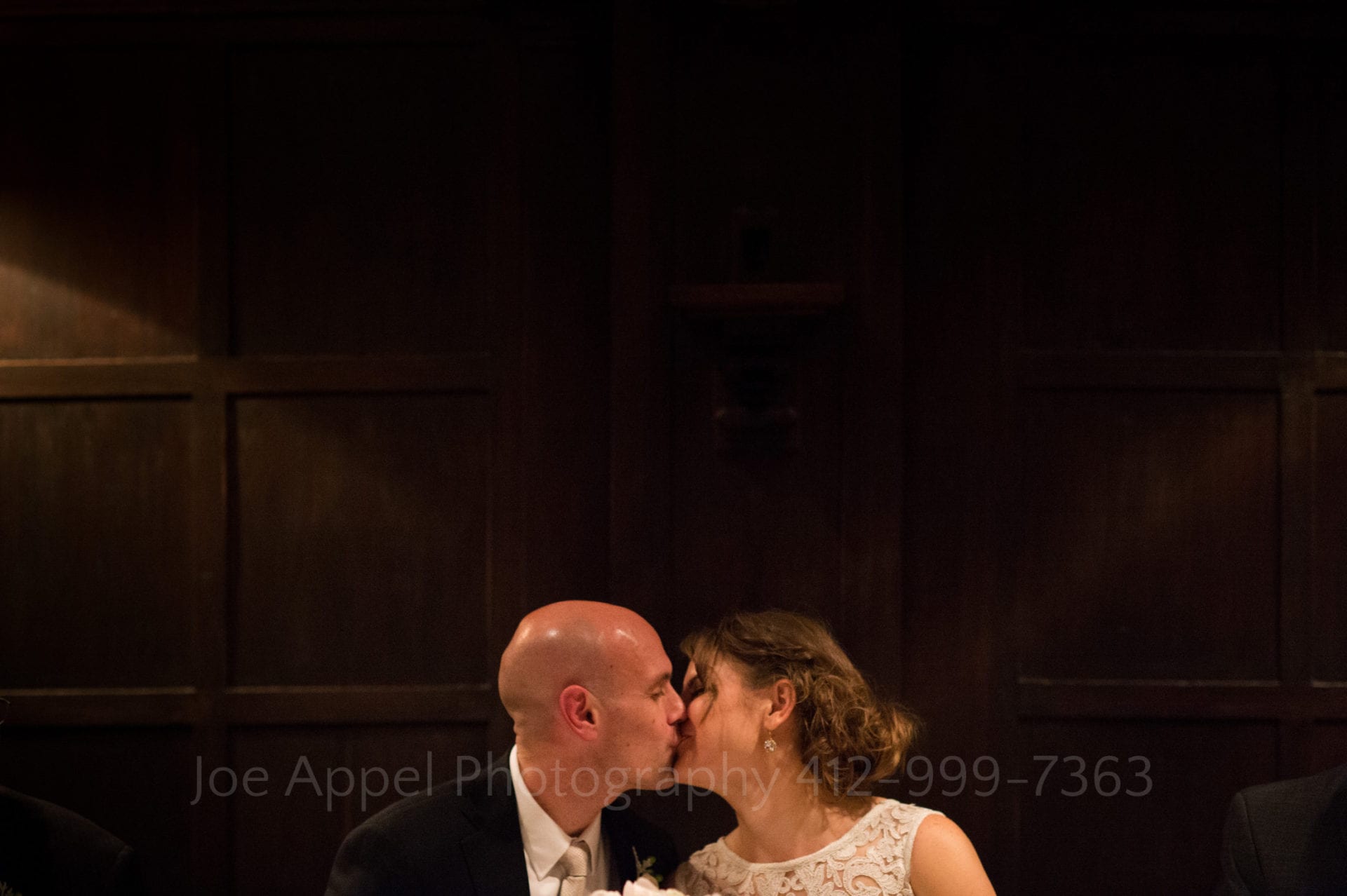 a bride and groom kiss in front of a brown wooden wall