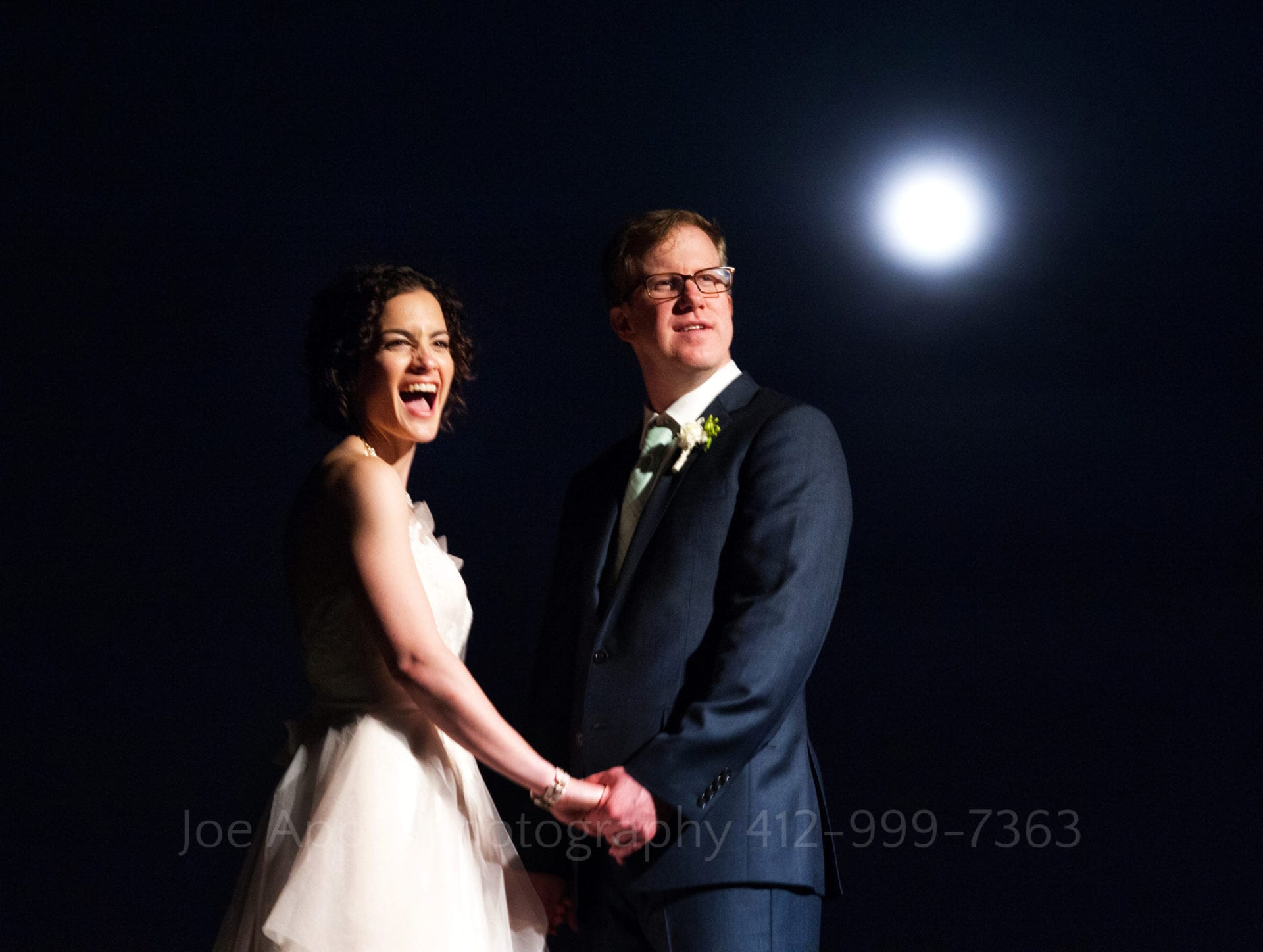 a bride and groom hold hands and smile with the moon behind them