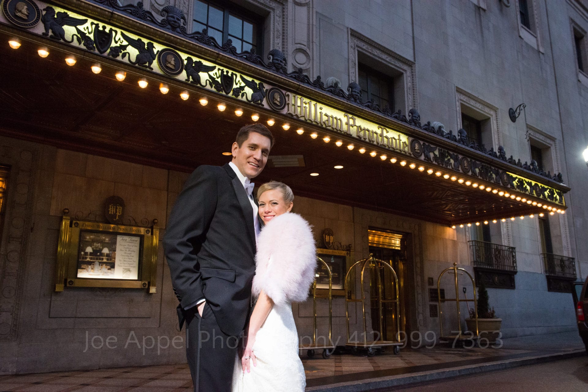 a bride and groom stand in front of the entrance to the william penn hotel