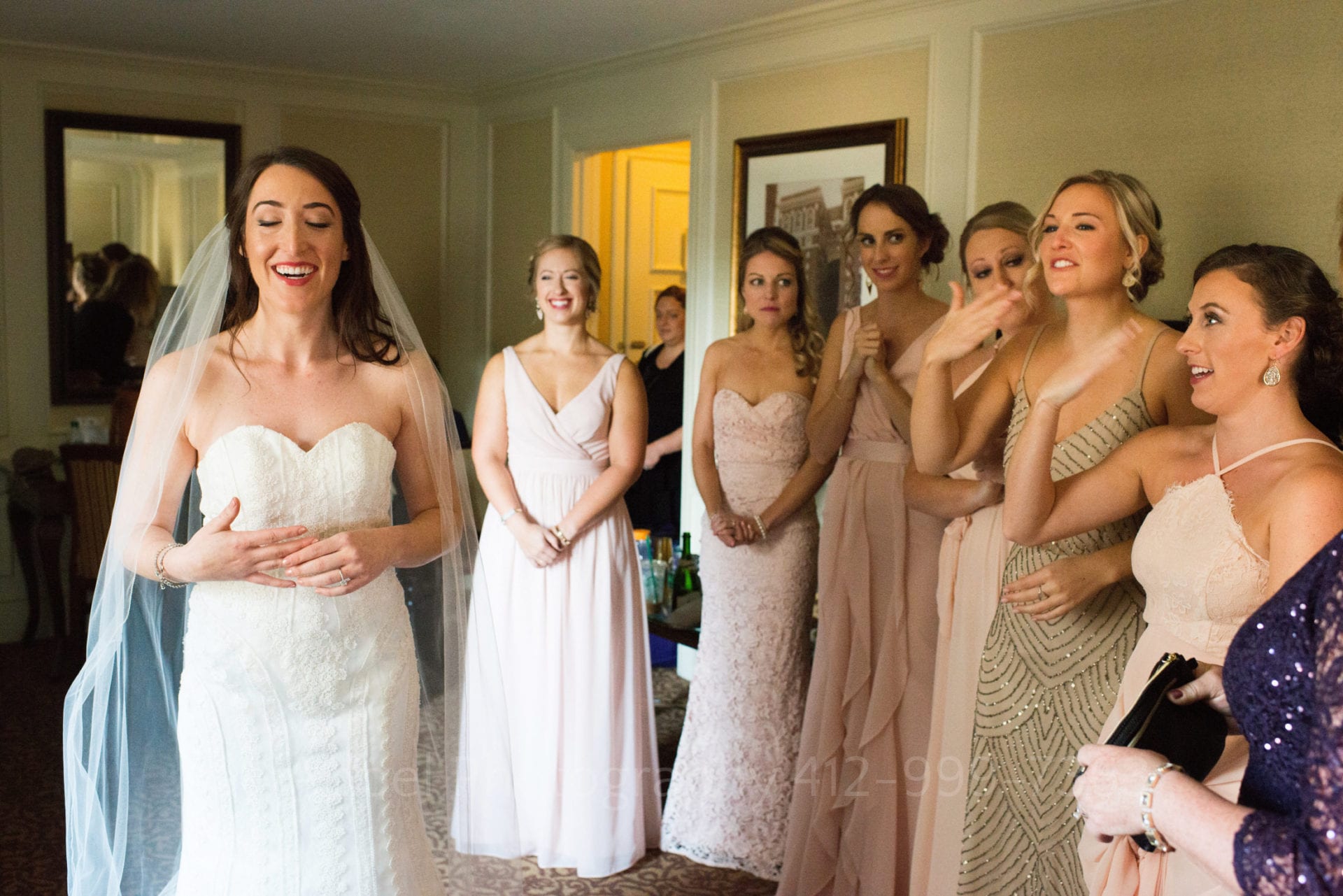 bridesmaids in blush pink dresses smile and cry as they look at the bride
