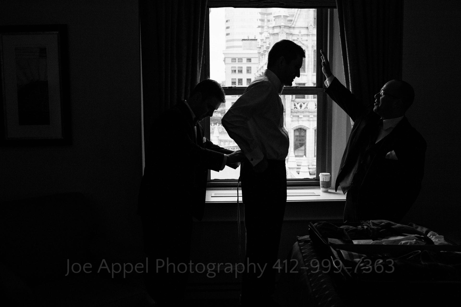 a grooms father ties his belt in front of an open window