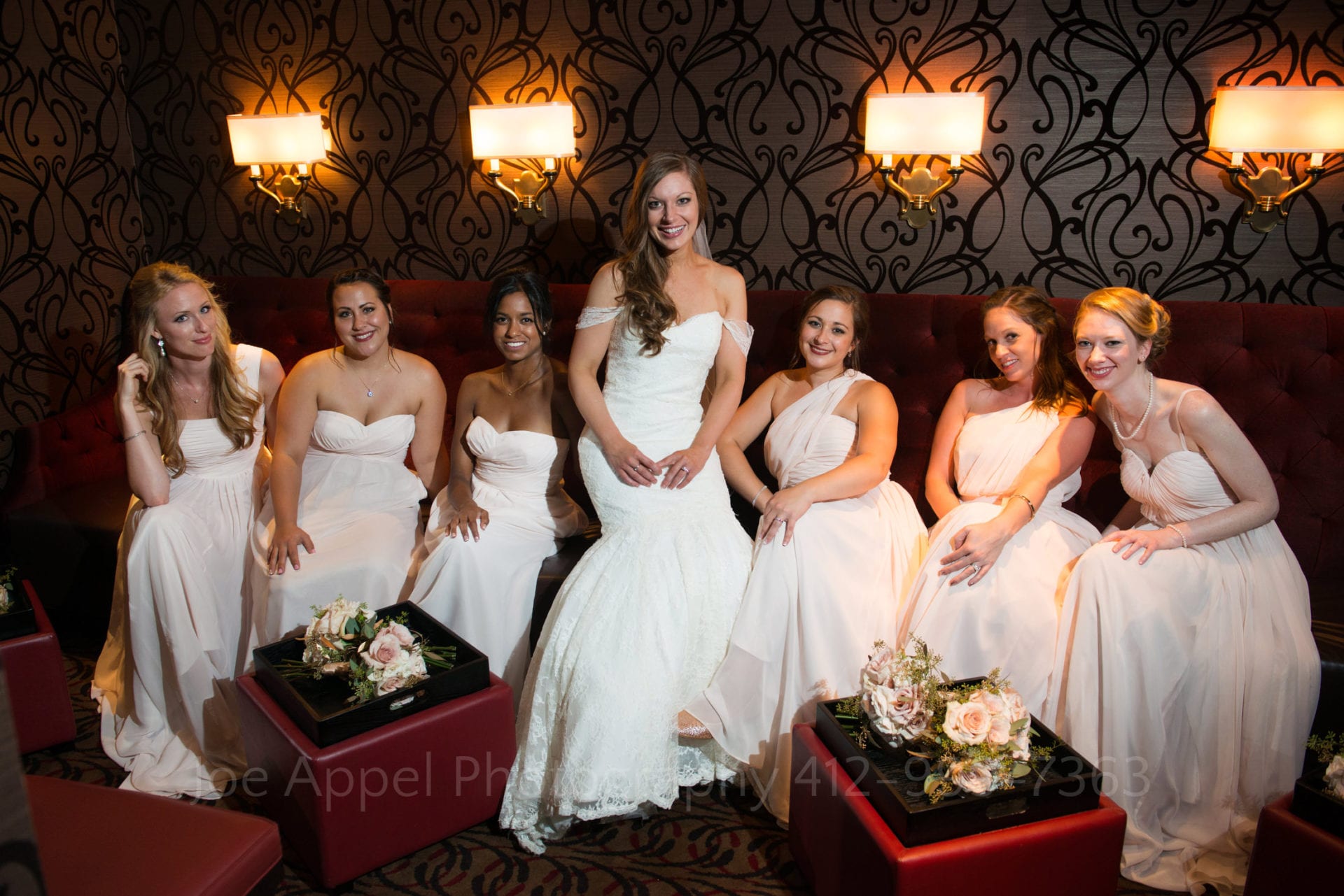 a bride and her bridesmaids pose on a maroon couch