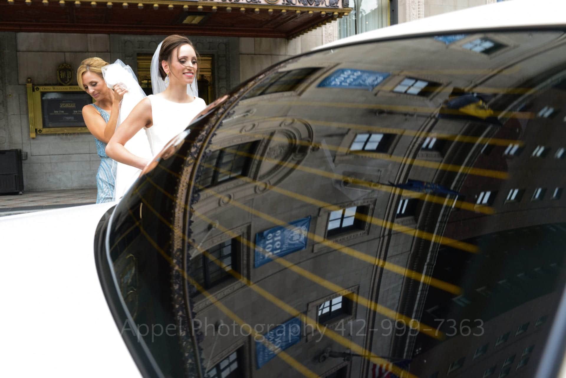 a woman holds a brides skirt as she steps into a car
