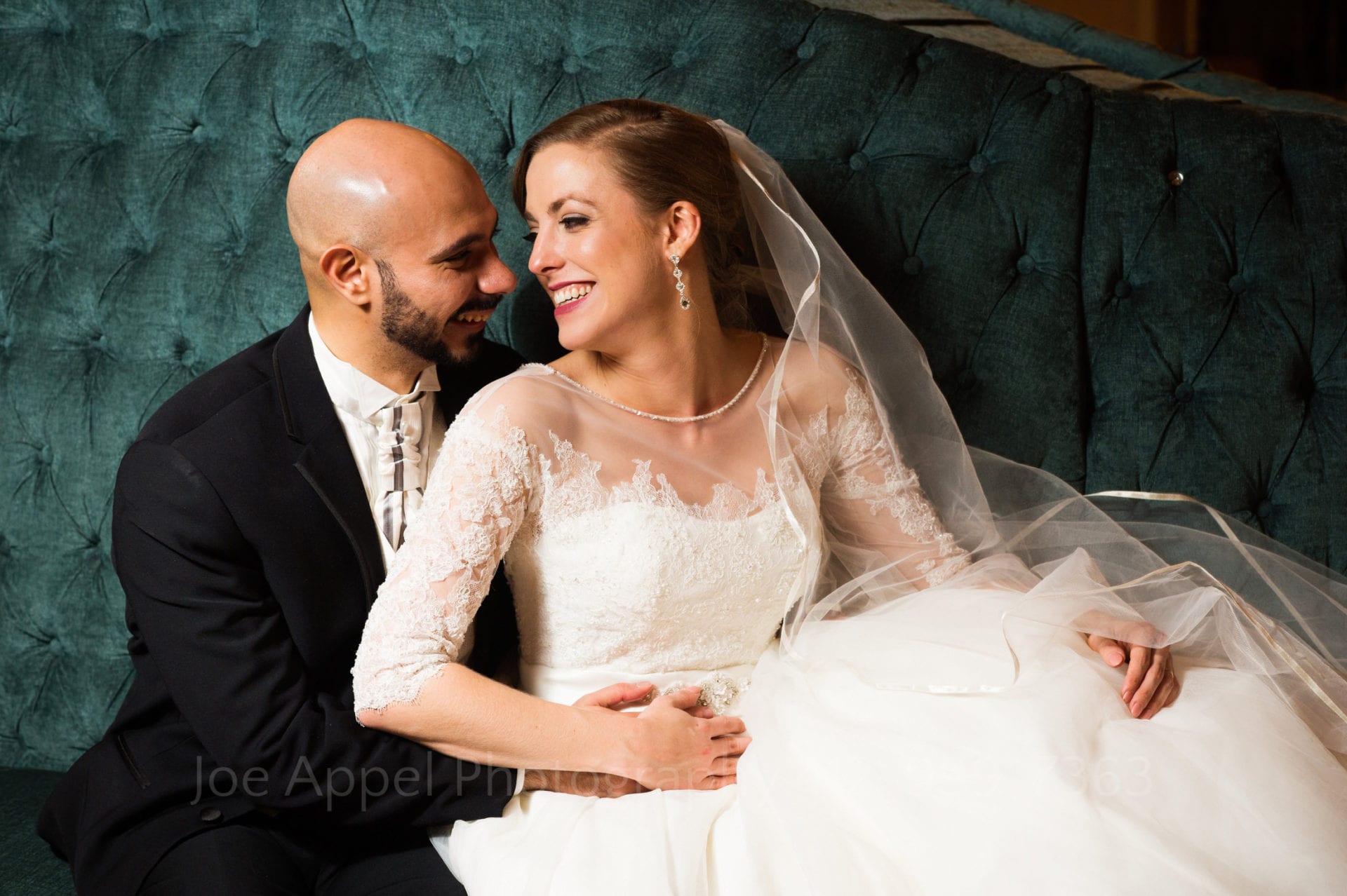a bride and groom sit on a teal couch together