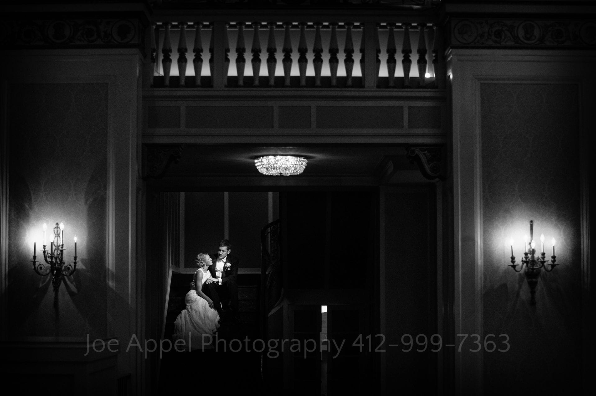 a bride and groom sit on a dark staircase together