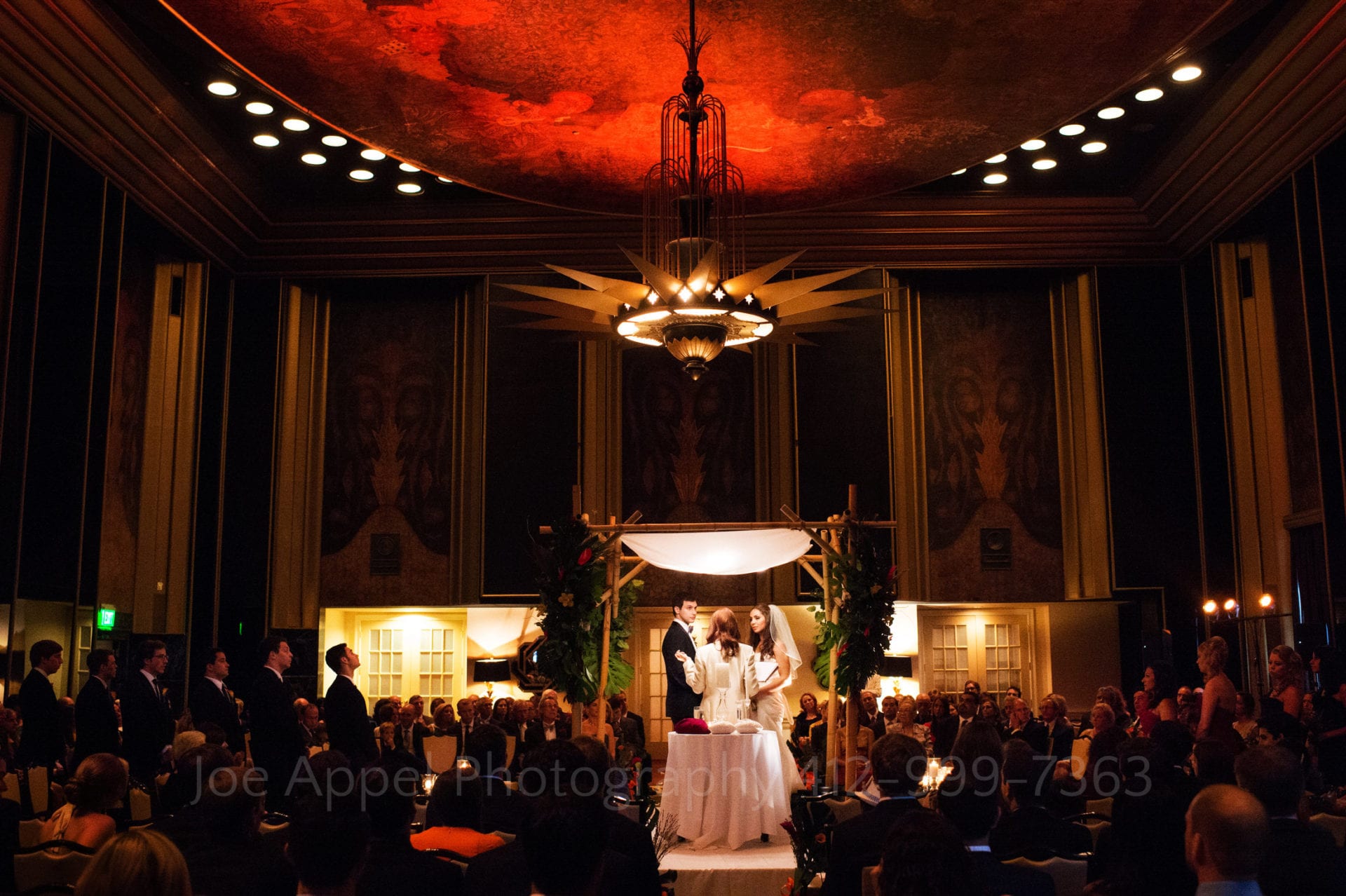 a bride and groom stand under their chuppah in an illuminated red room