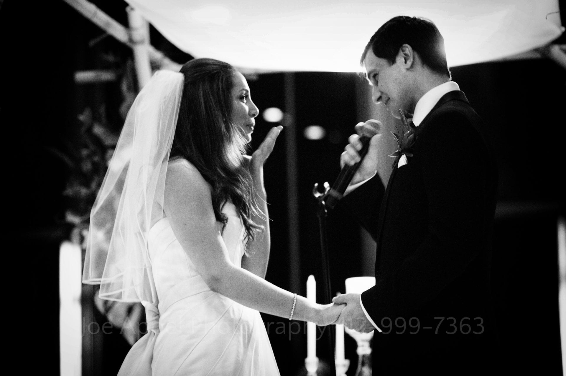 a bride blows a kiss at her groom as he speaks into a microphone