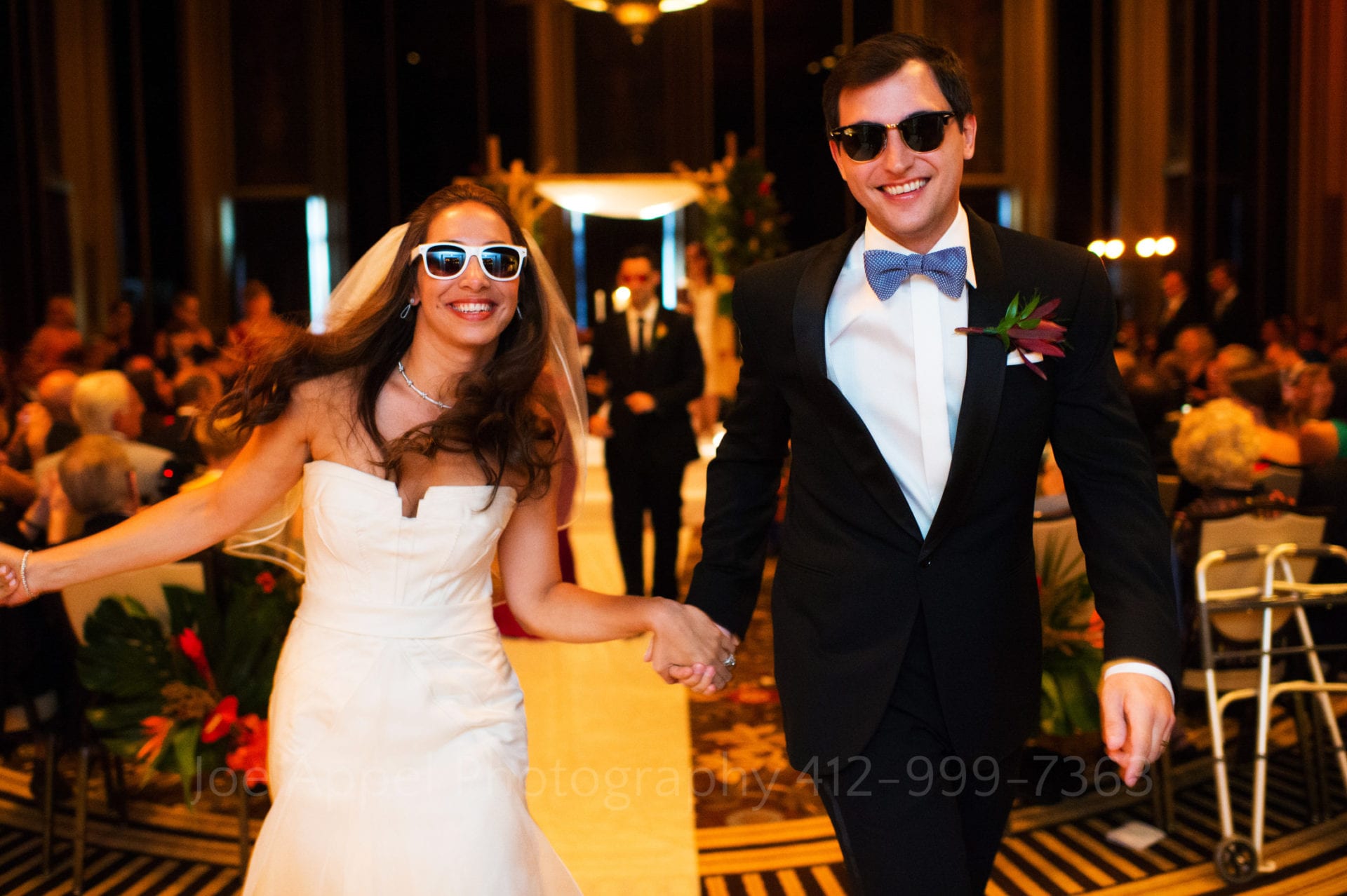 a bride and groom wearing sunglasses walk down the aisle holding hands