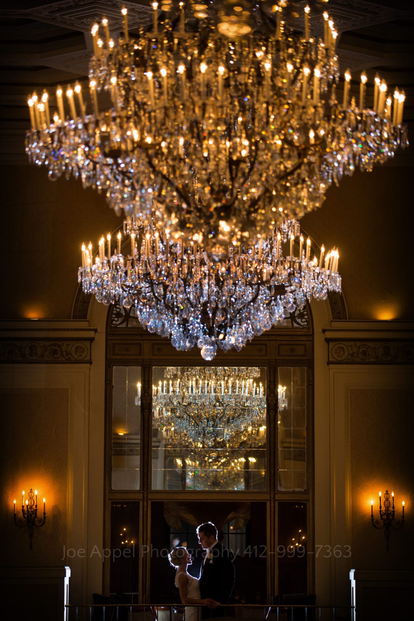 a bride and groom stand under a crystal chandelier