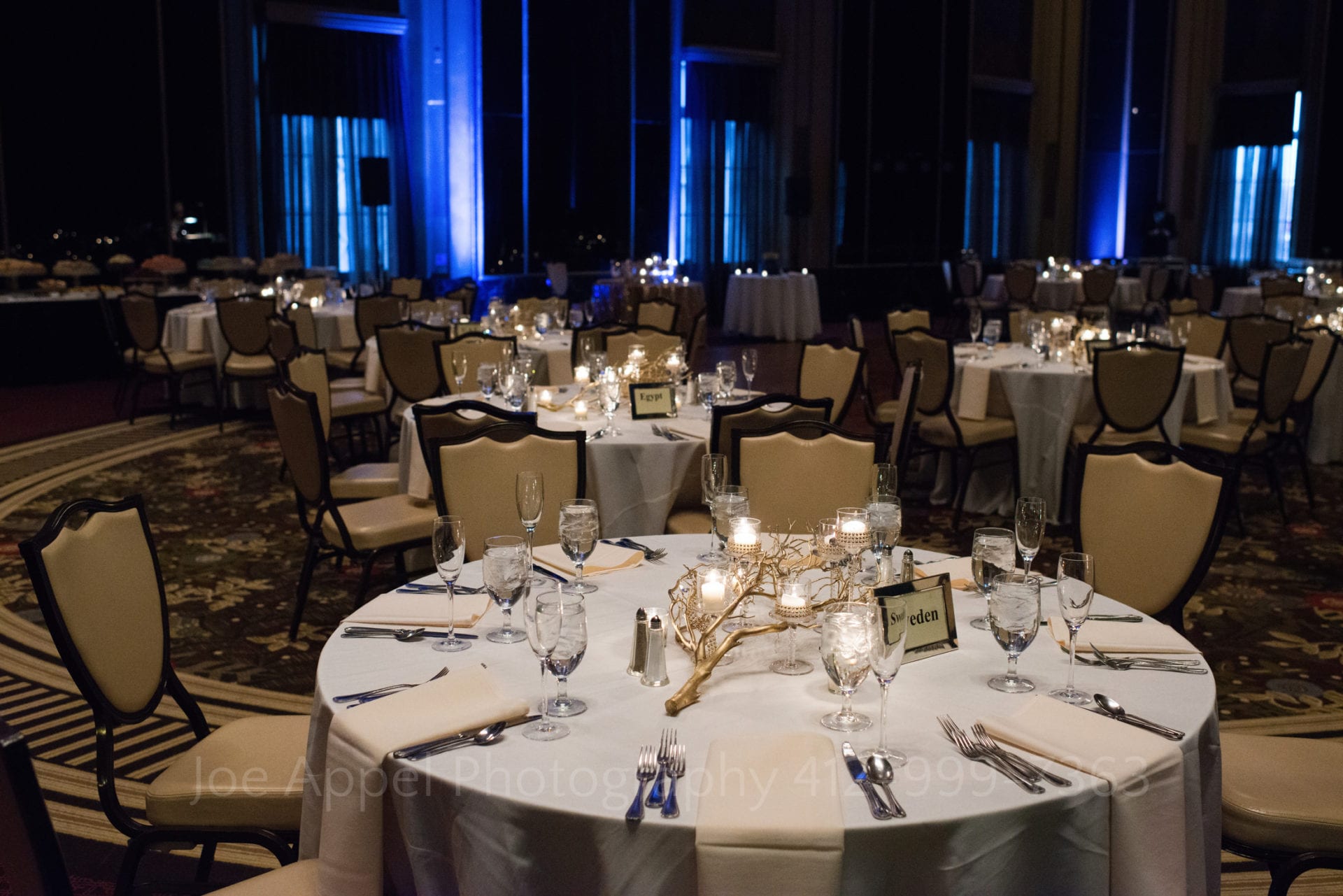 white dining tables with gold branch centerpieces and blue lights