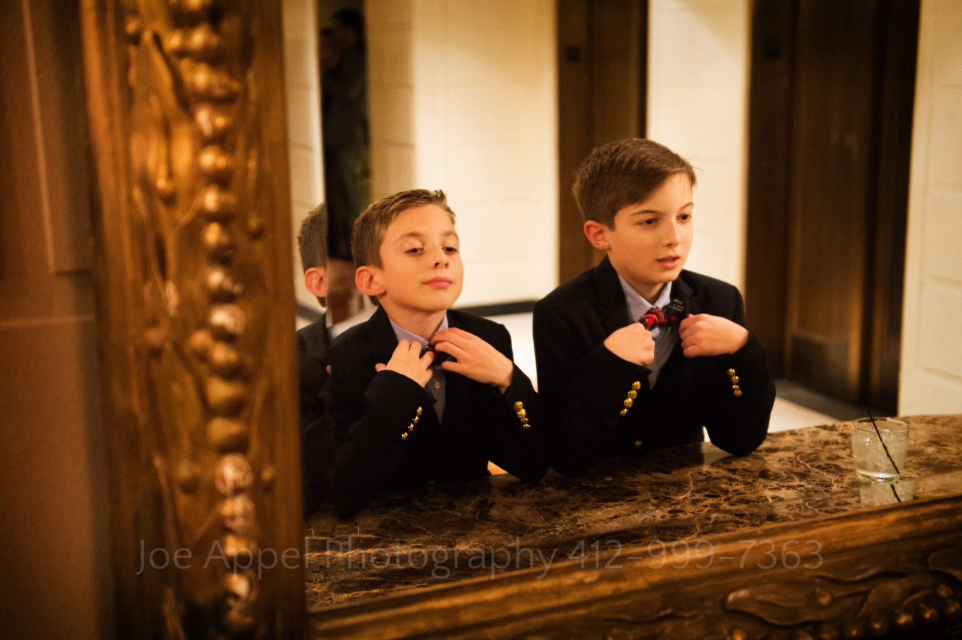 two little boys adjust their bowties in a mirror