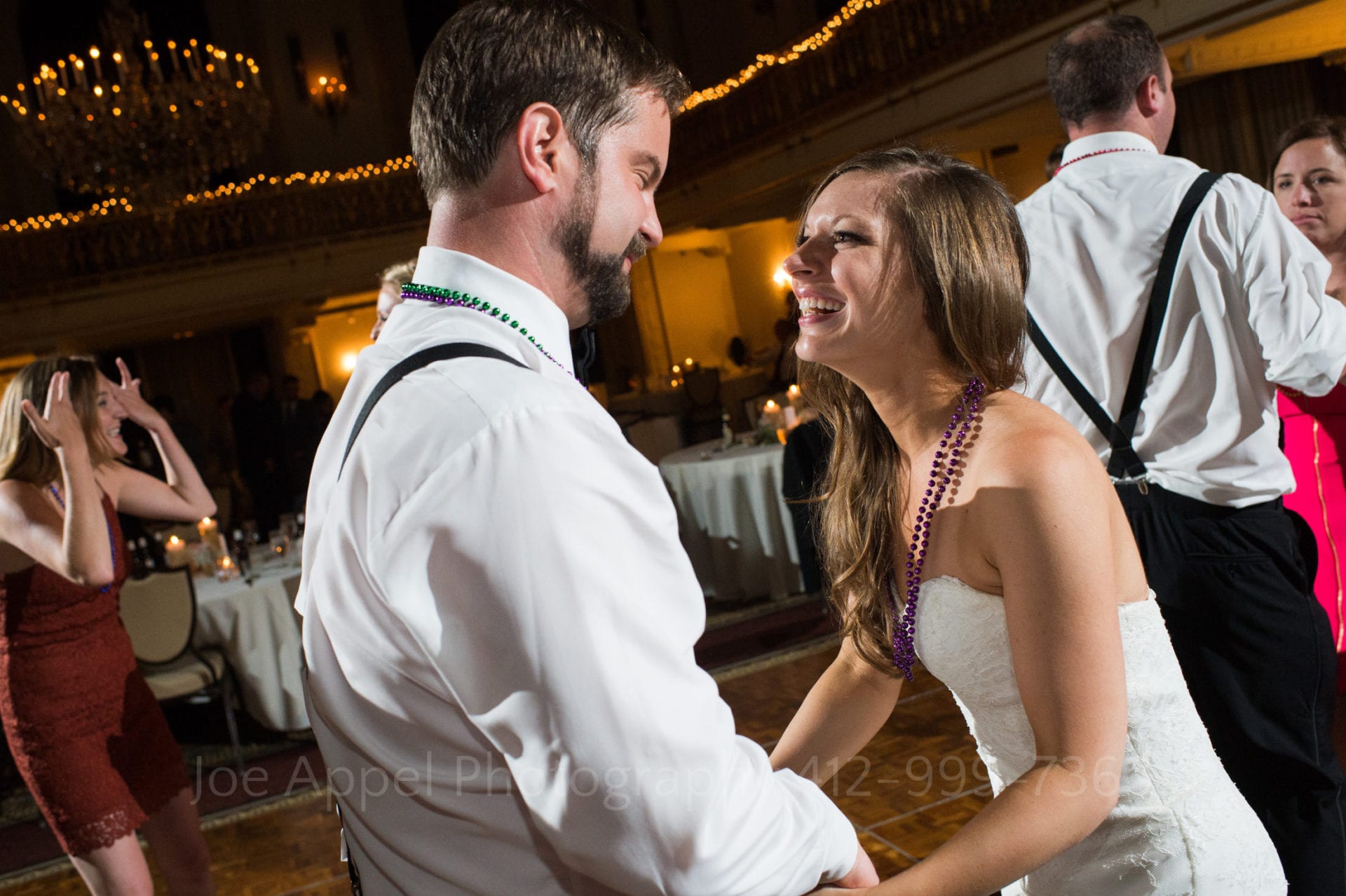 a bride and groom wearing mardi gras beads laugh and dance