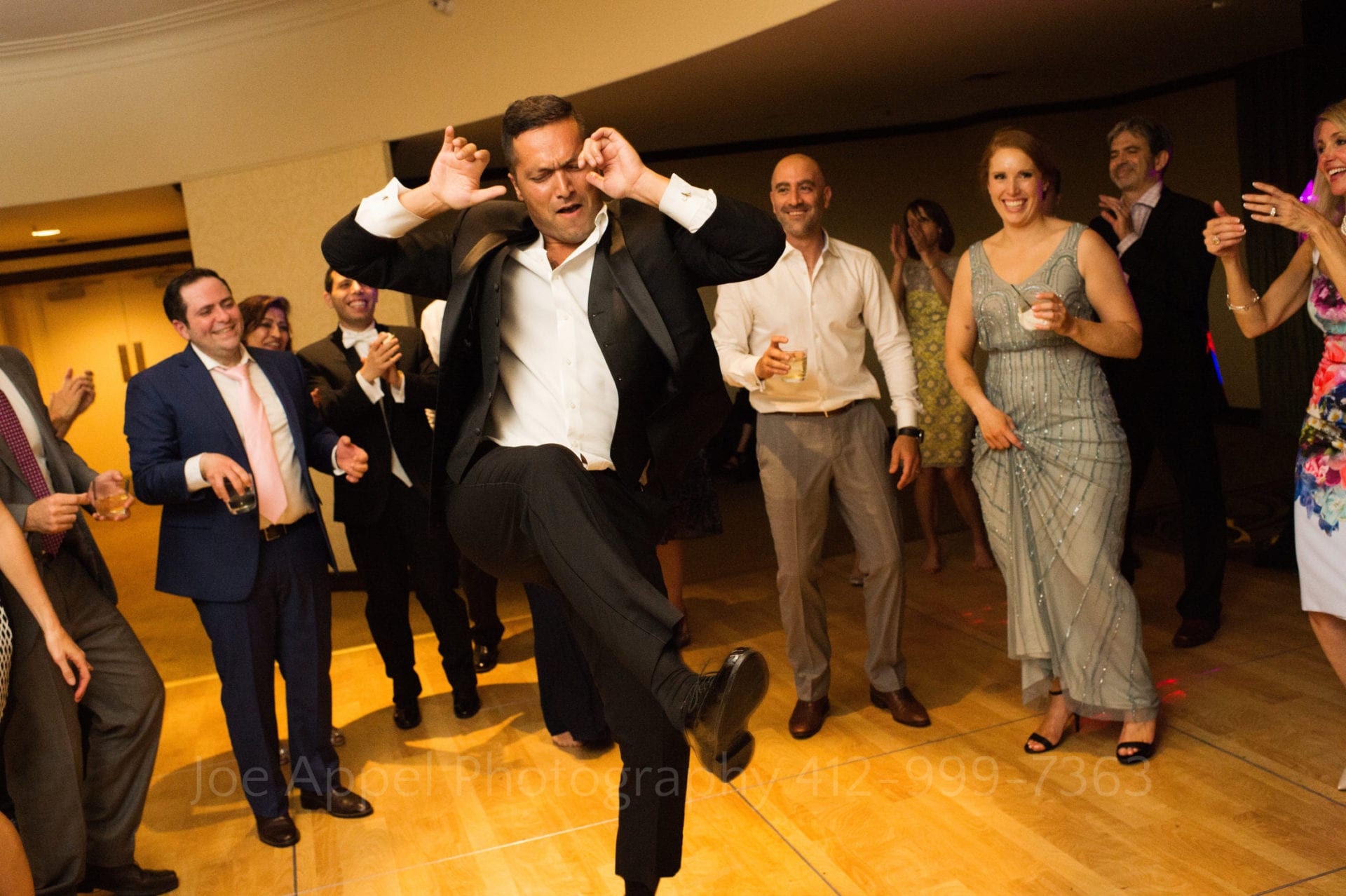 a man in a suit dances as guests laugh and watch
