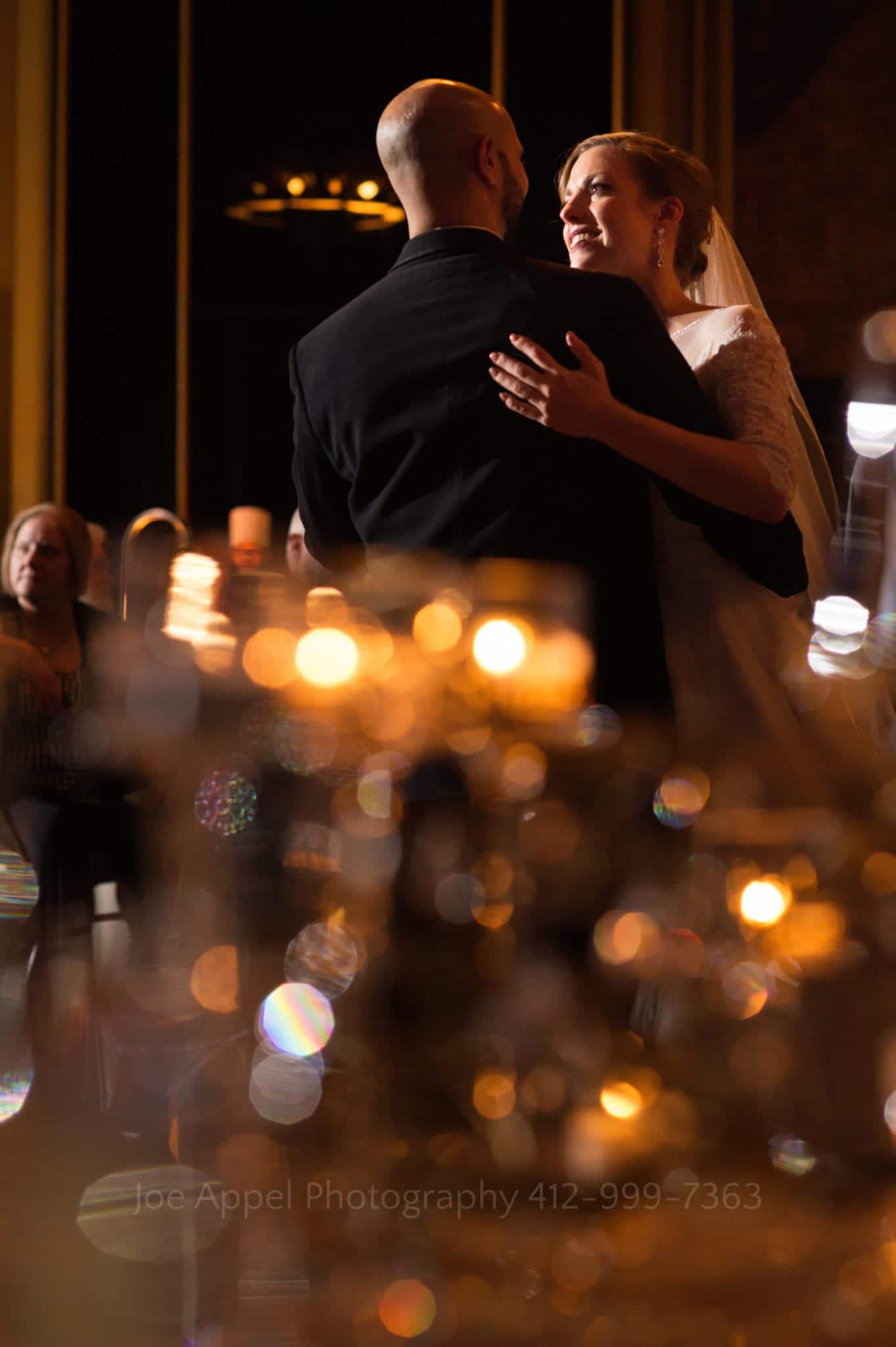 a bride and groom smile and dance in an illuminated room