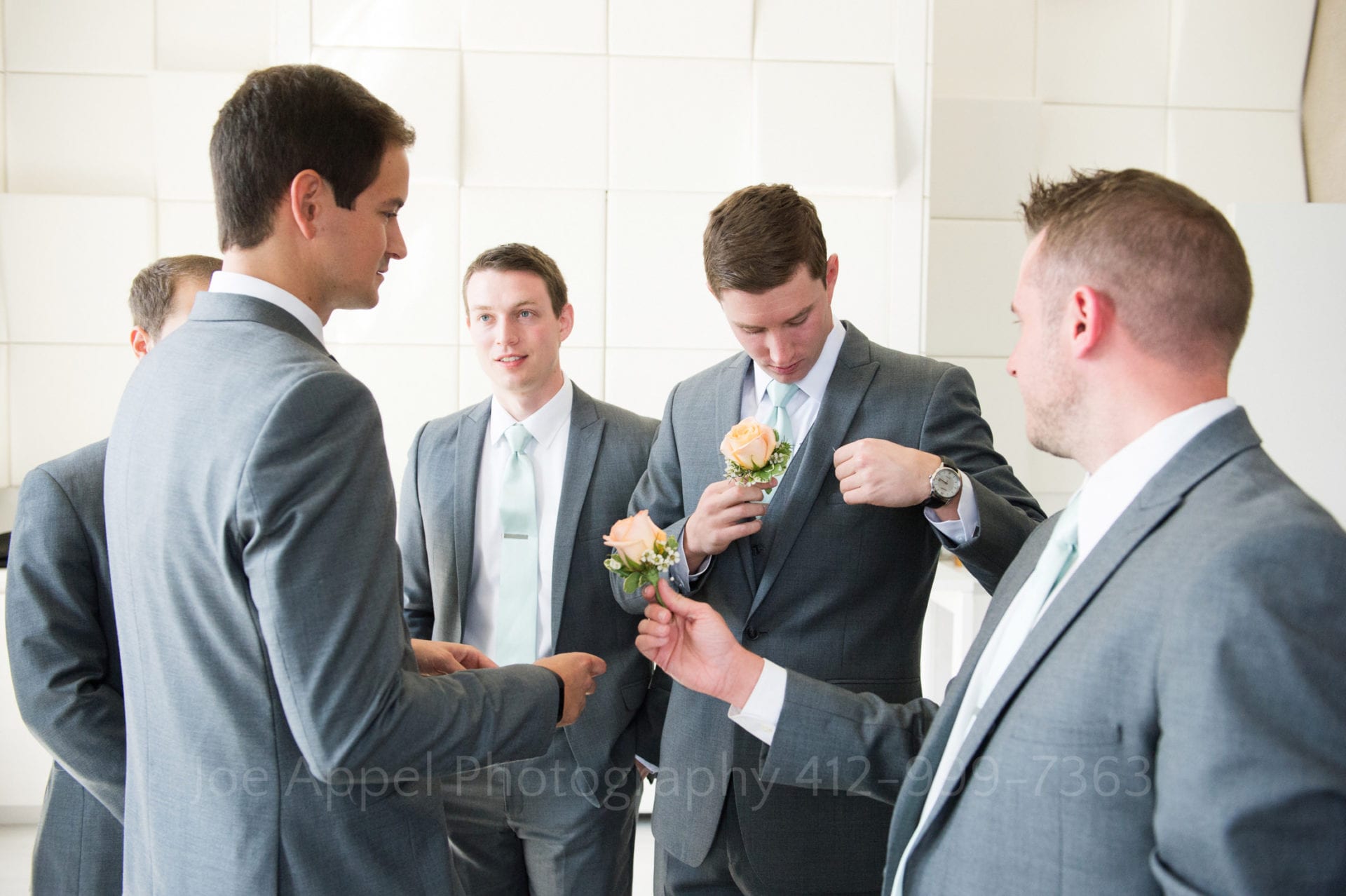 a groom and his groomsmen fasten orange roses on his suit