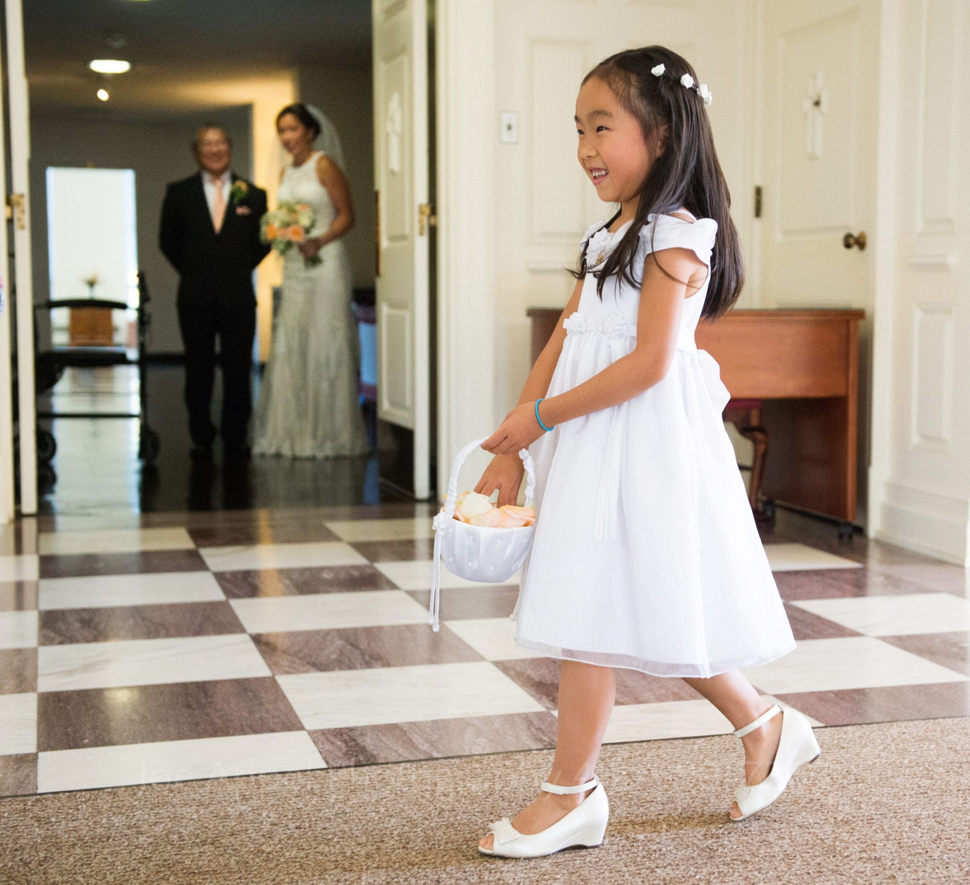 the bride and her father watch a smiling flower girl walk down the aisle with orange flower petals