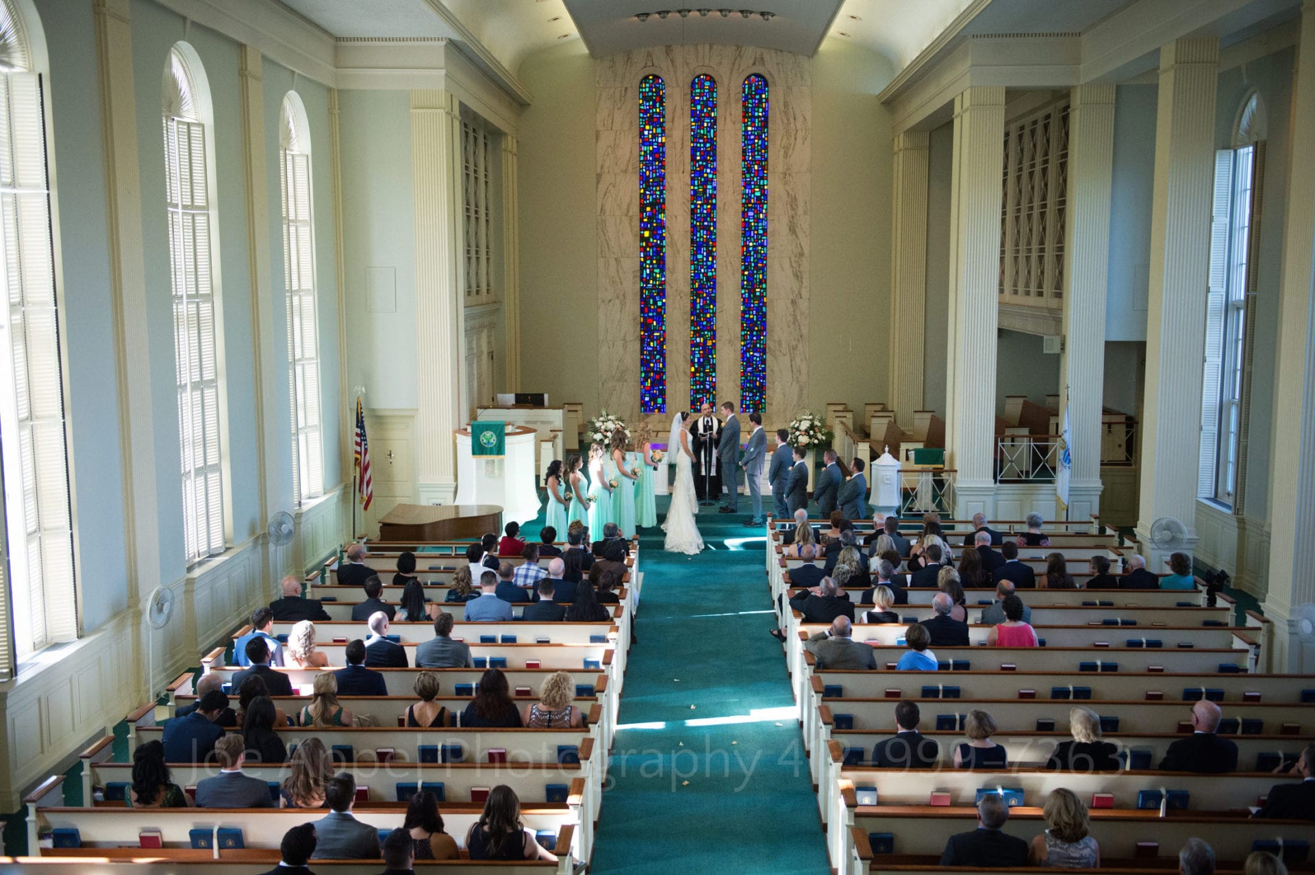 guests sit in the chapel and watch the bride and groom say their vows in front of colorful stained glass windows