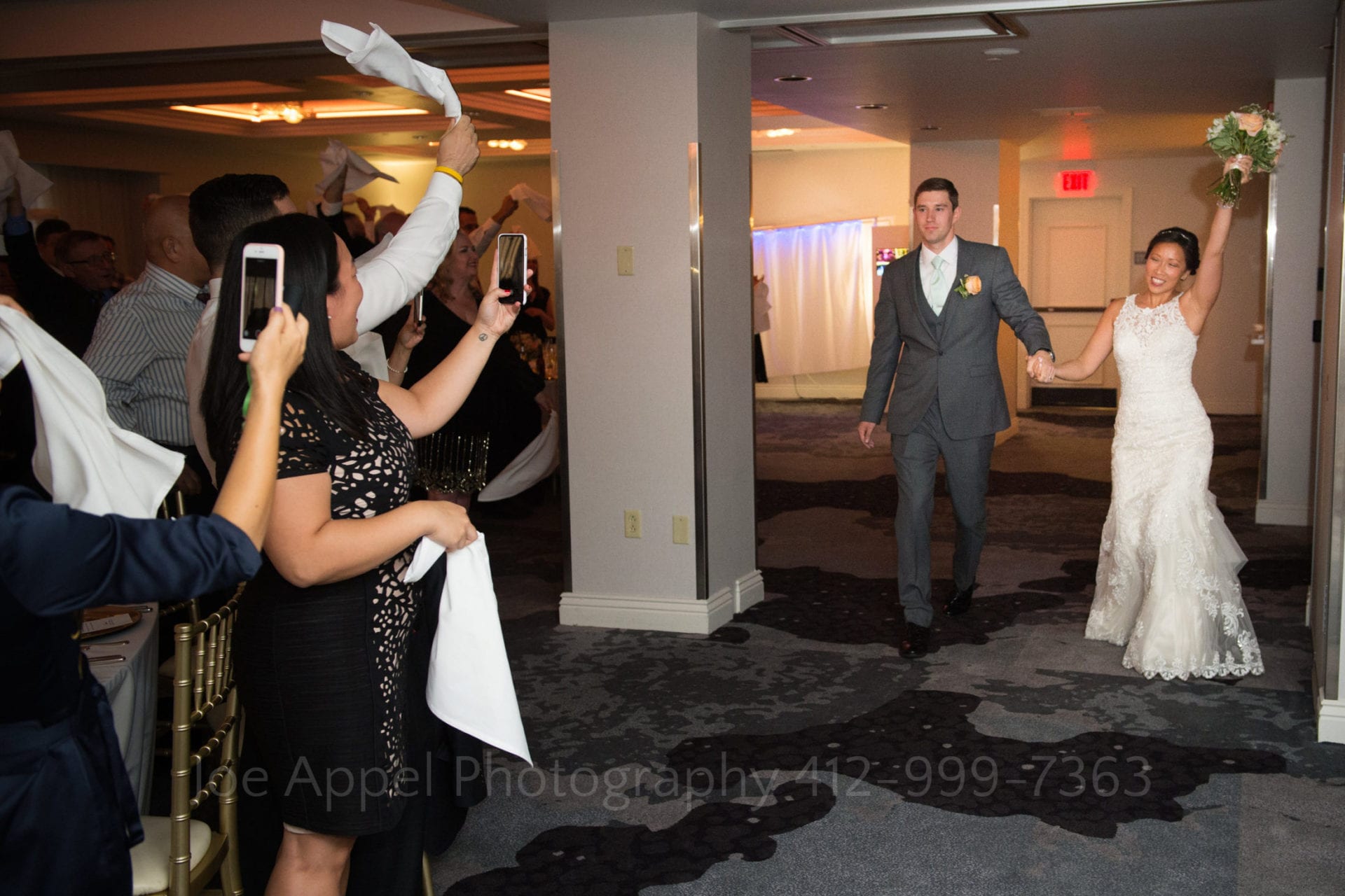 guests cheer and take photos as the bride and grrom enter the reception area
