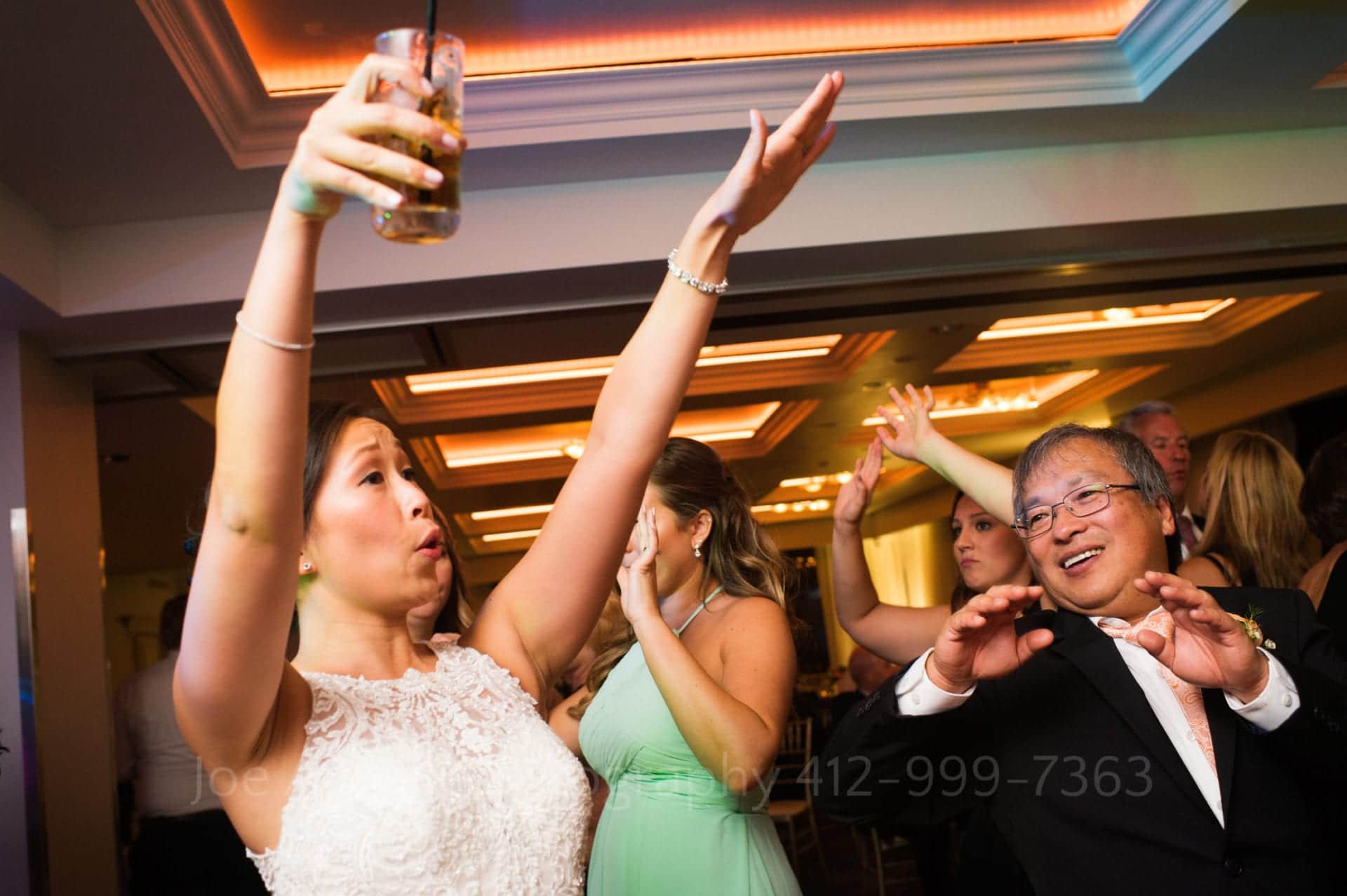 a bride holds a drink and dances with her father