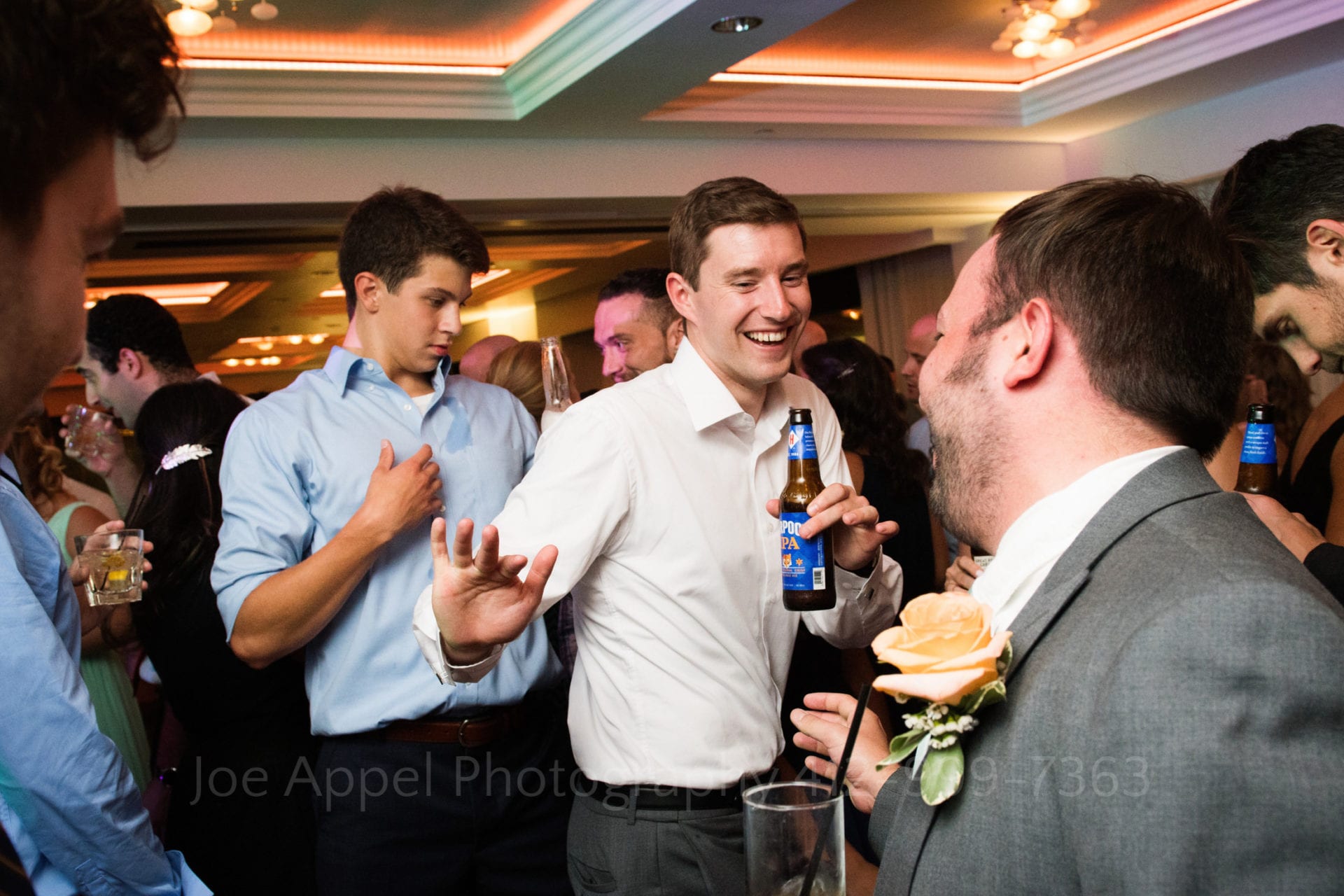 a groom holds a beer and dances with friends