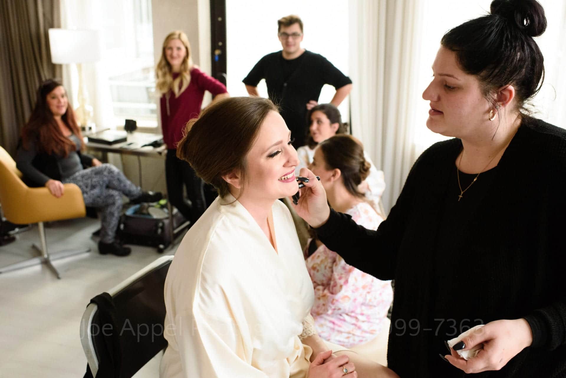 a bride smiles as a makeup artist applies her foundation