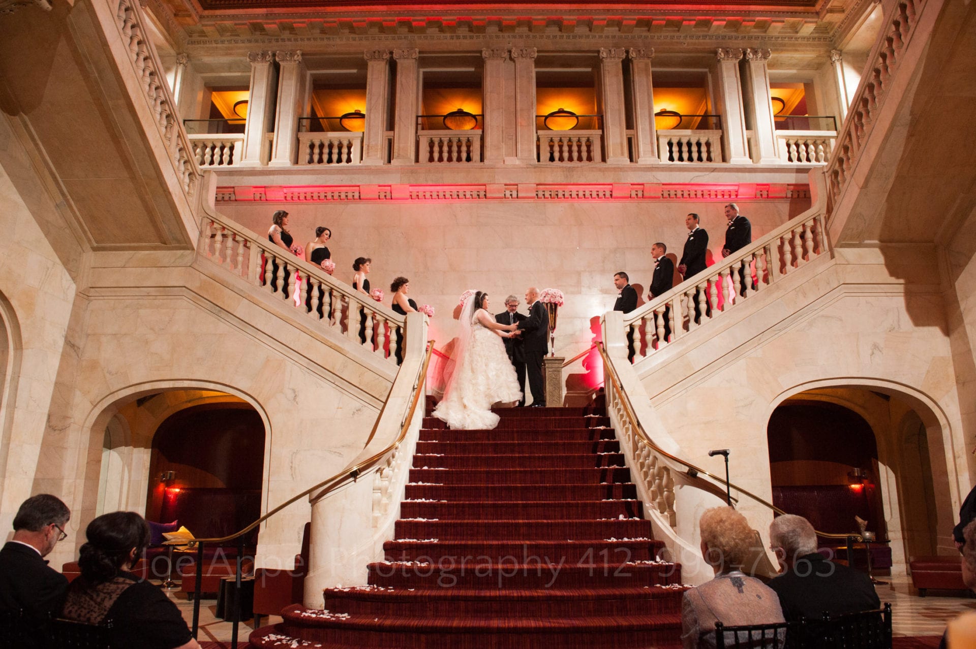 a bride and groom say their vows on a red staircase with pink lights and flowers - the grand staircase is a great spot for renaissance hotel pittsburgh weddings
