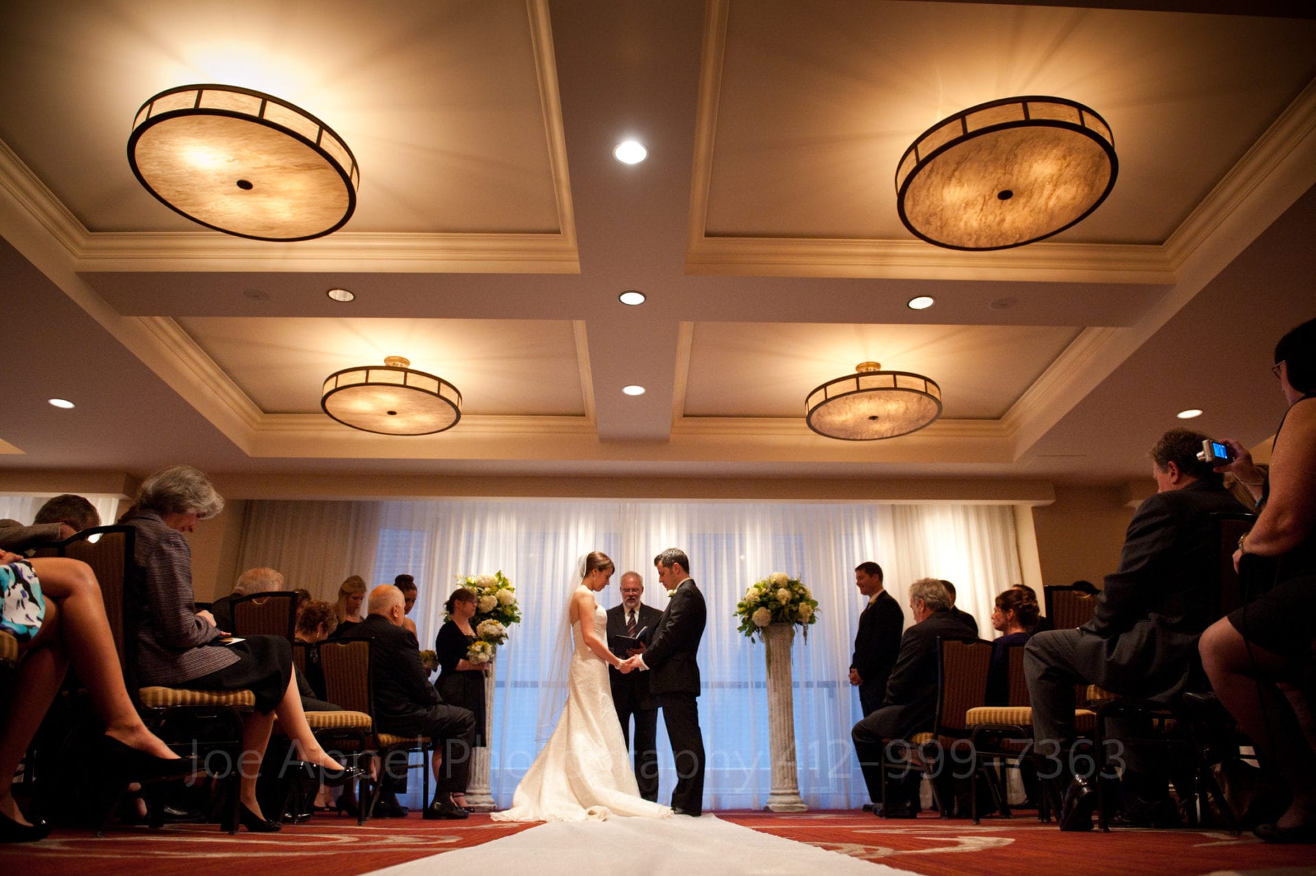 a bride and groom say their vows in a room with white ceilings and illuminated lights