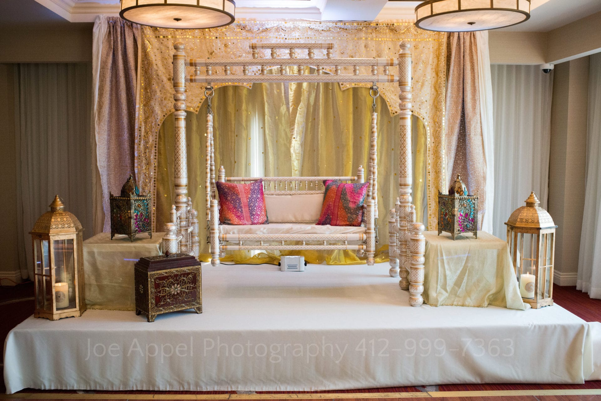 a white and gold jhula with colorful pillows and ornamental boxes