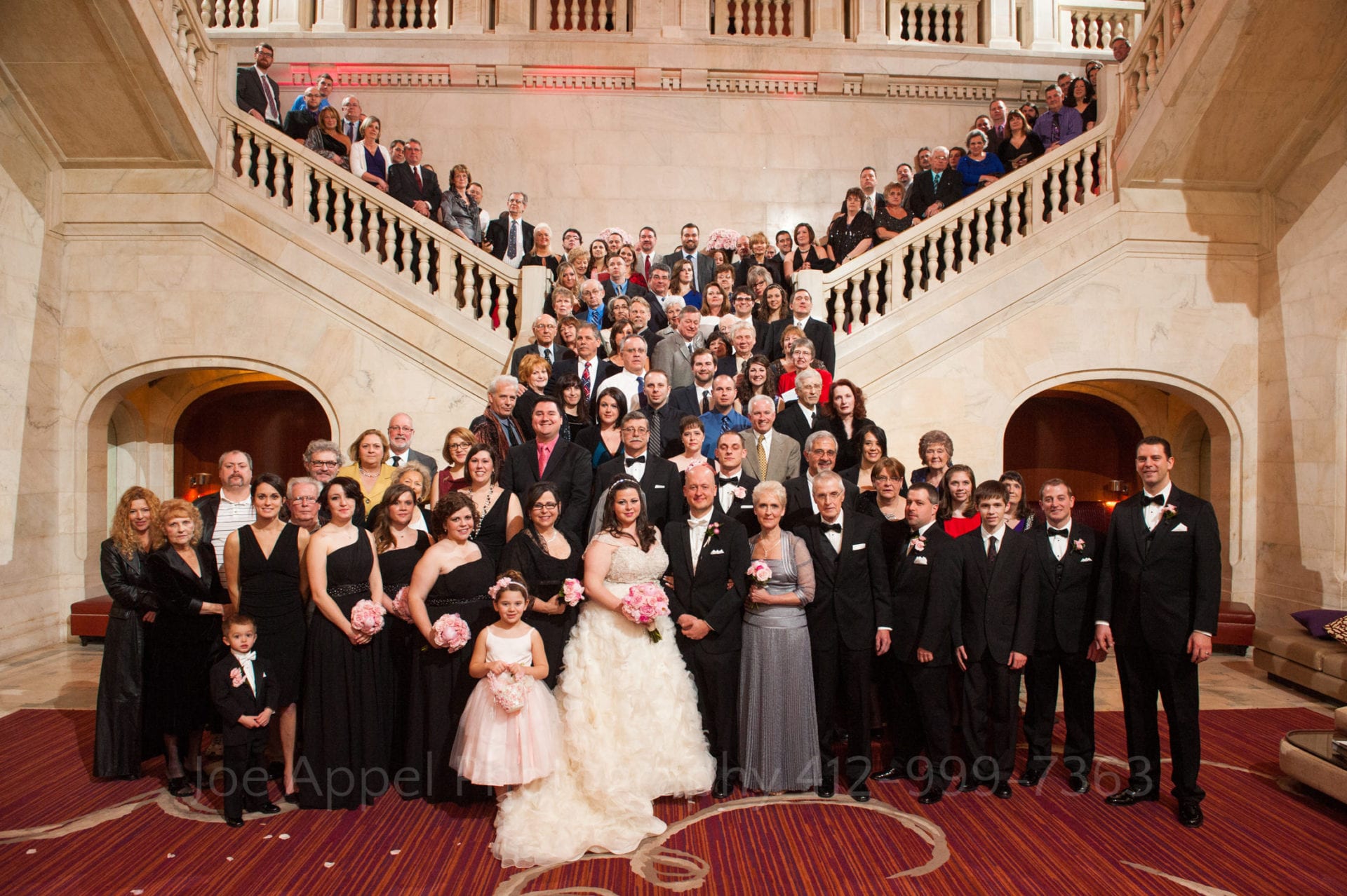 the wedding party and guests stand on a red carpeted staircase