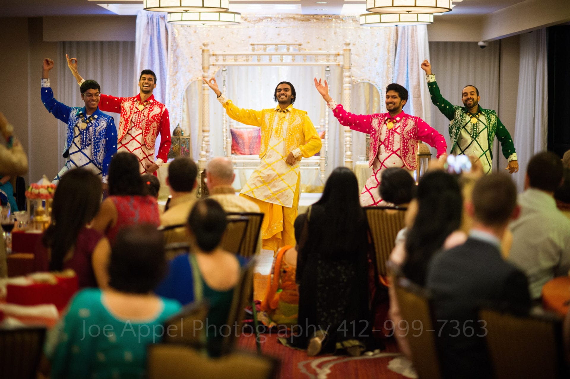 men in colorful kurtas dance for guests
