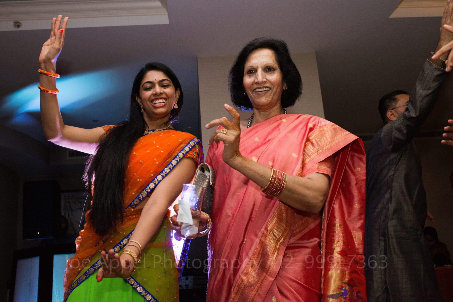 a woman in a green and orange sari dances with a woman in a pink sari