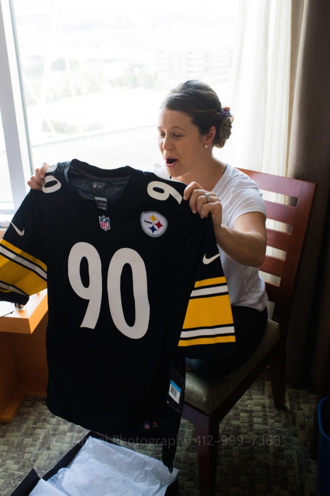 A woman holds up a number 90 Pittsburgh Steelers jersey with a look of joy and surprise on her face.