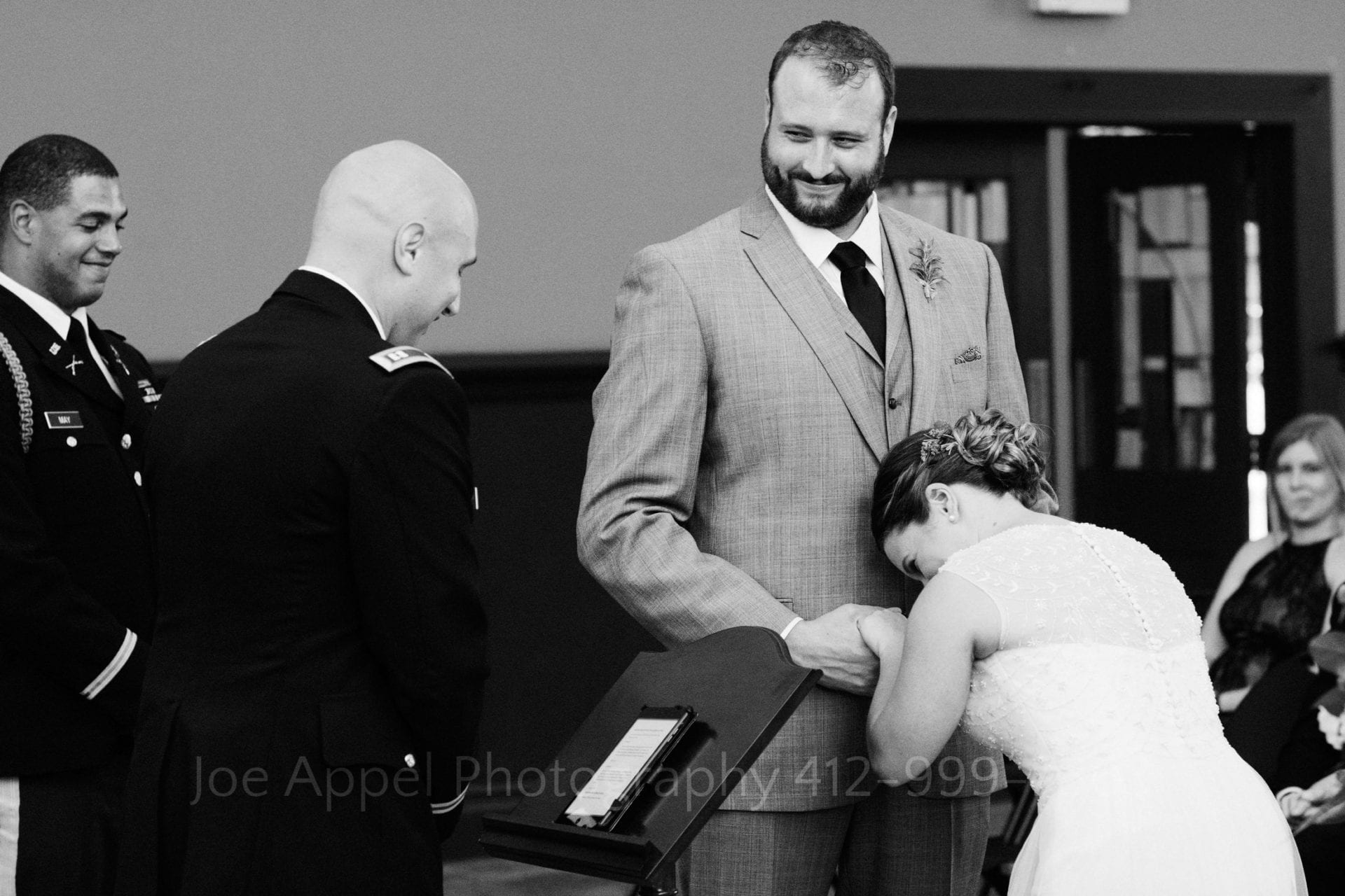 A groom looks over at the officiant and smiles as his bride bows her head in laughter.