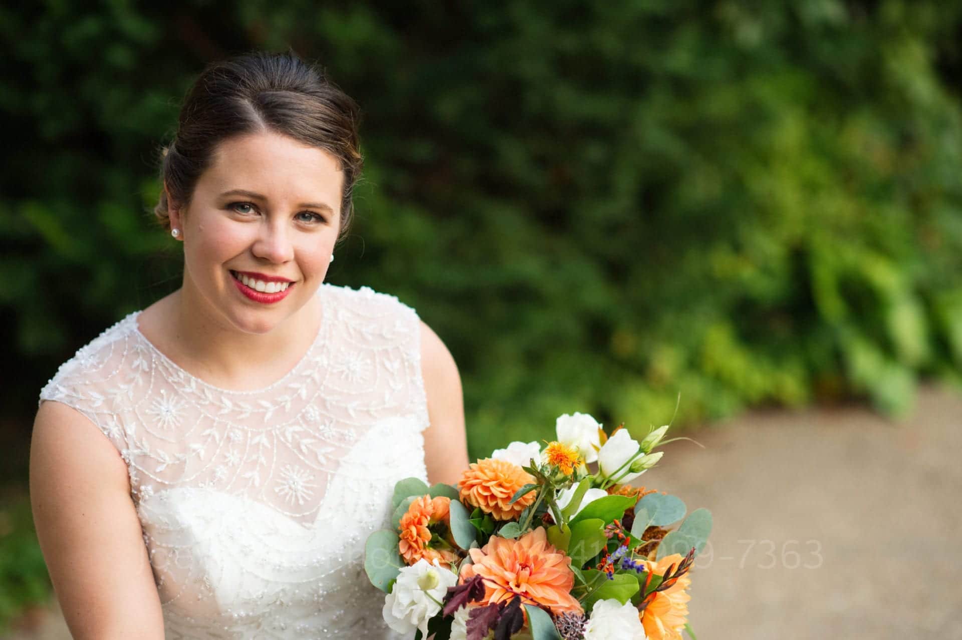 Portrait of a smiling bride holding a bouquet with an out of focus green background.